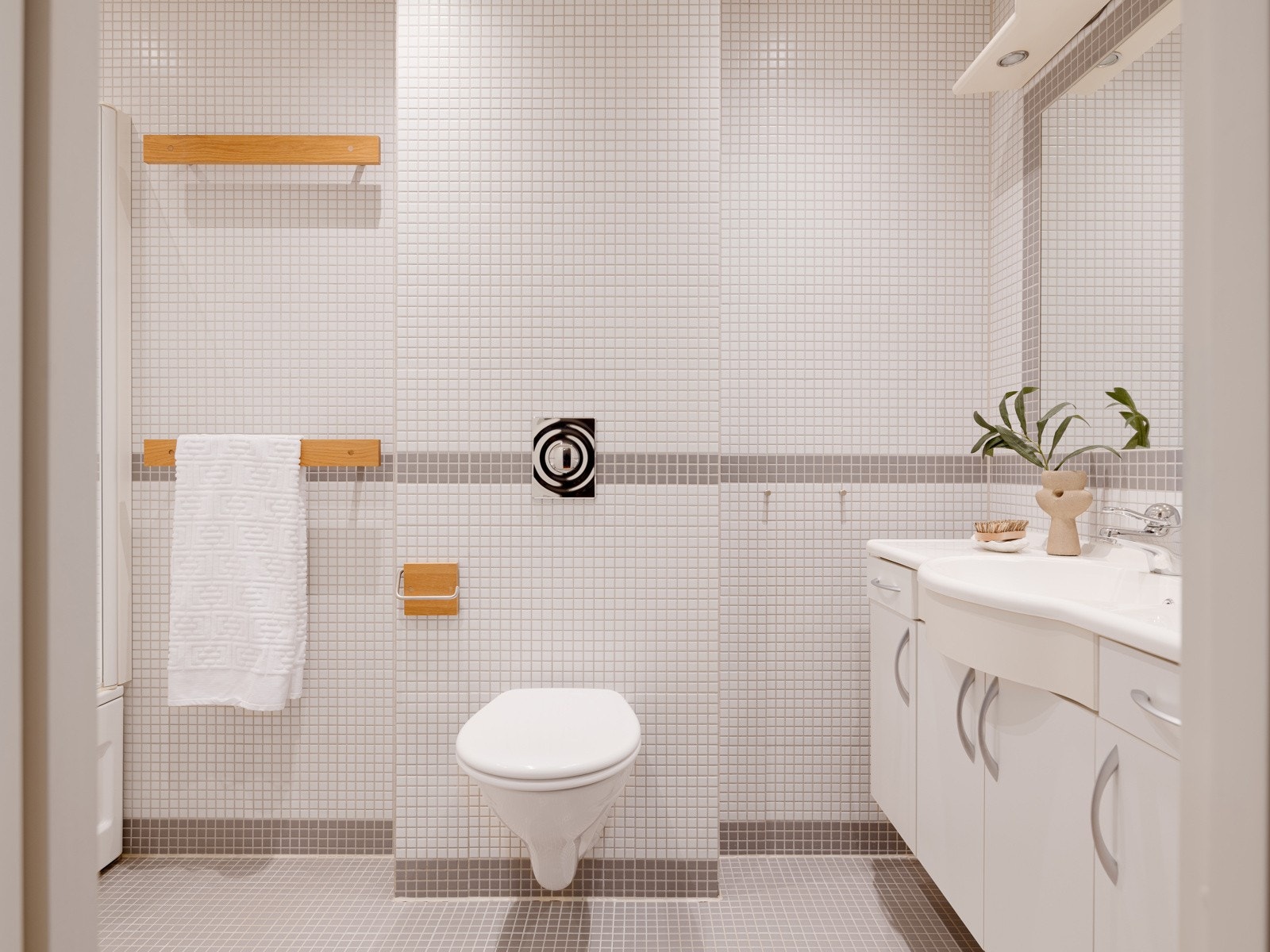 Badet med adkomst direkte fra soverommet fremstår som en praktisk og privat løsning, med helflisede overflater i et nøytralt uttrykk, slett malt himling med downlights og elektriske varmekabler i gulv. Galleribilde