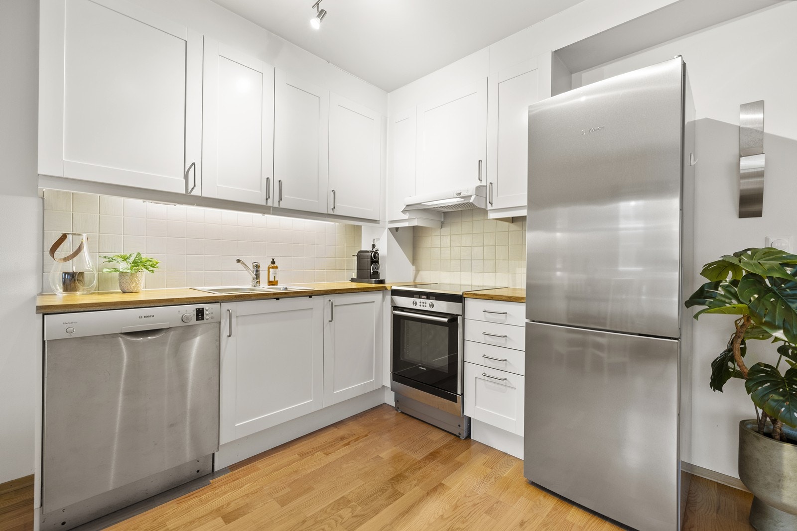 Kjøkkeninnredning med hvite fronter, benkeplate i tre og hvitevarer i rustfritt stål. Galleribilde