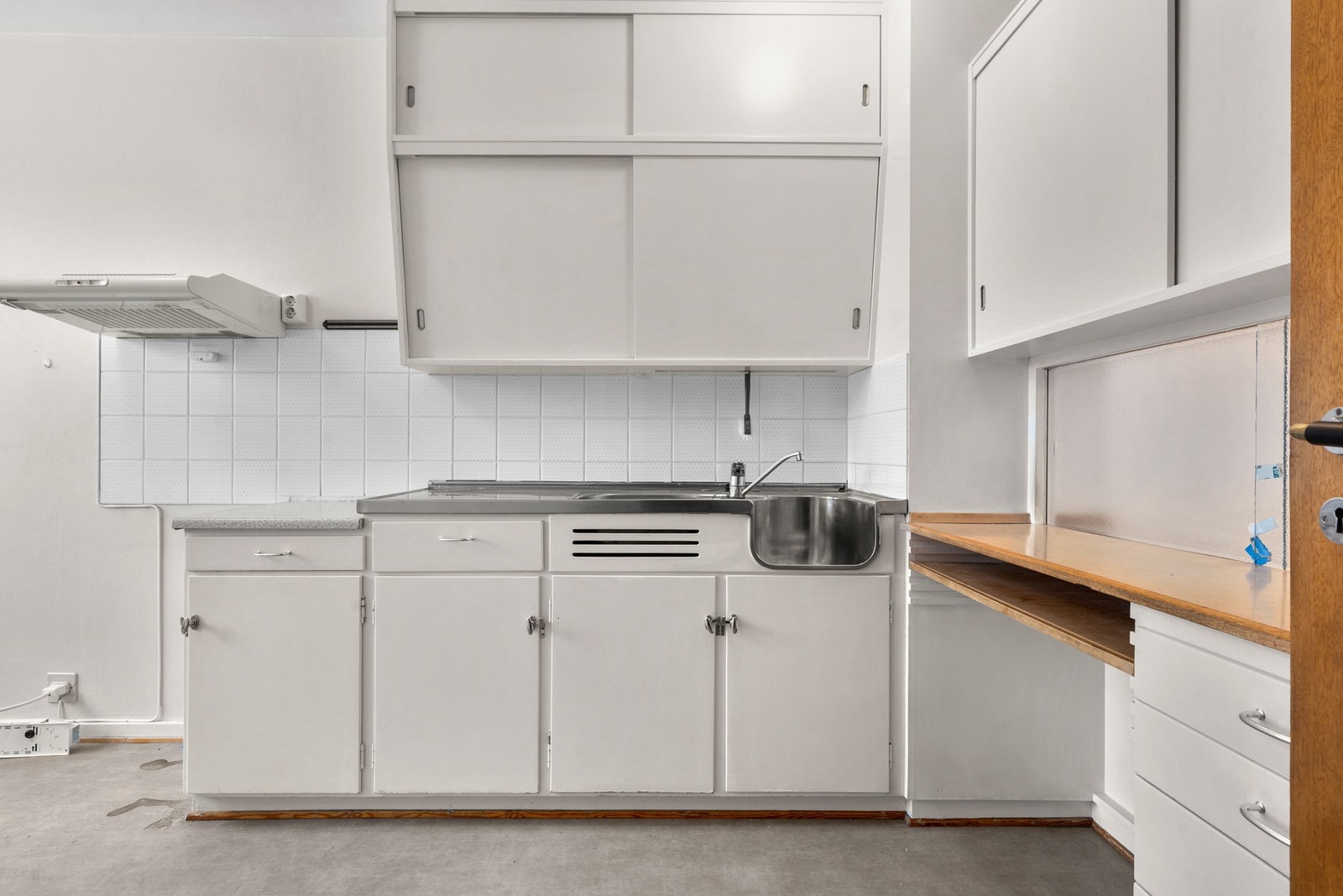 Kjøkkeninnredning med malte fronter, laminat benkeplater, heldekkende oppvaskkum, ventilator og
fliser over benk Galleribilde