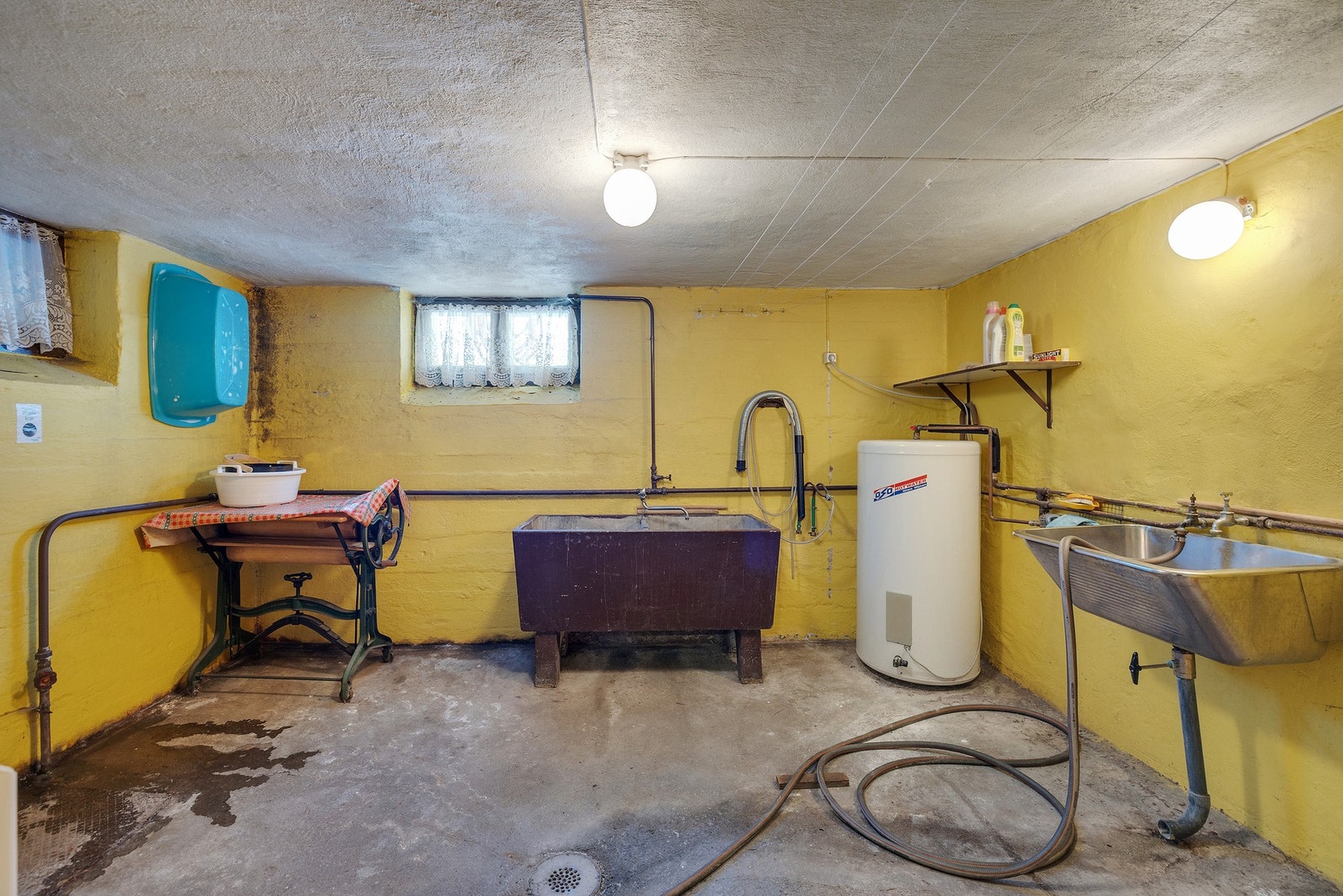 Vaskerommet fremstår som en typisk vaskekjeller fra byggeperioden, med betonggulv og eldre sluk i støpejern. Galleribilde