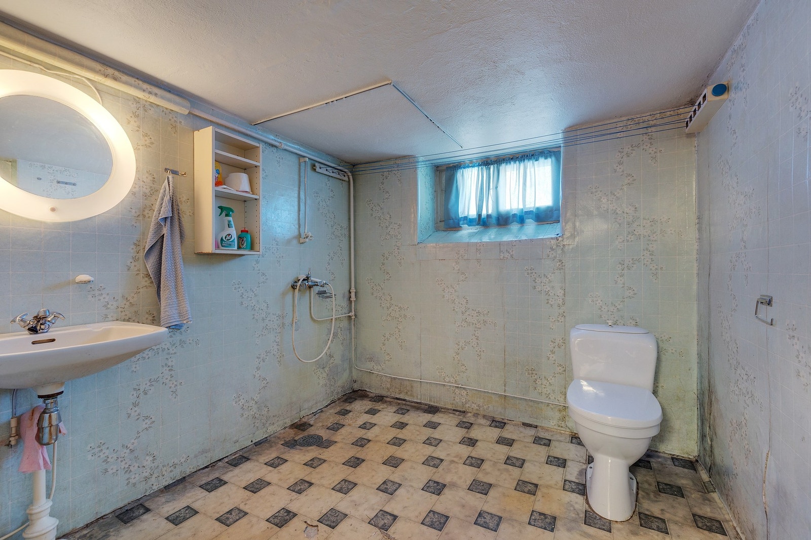 Badet er av eldre dato og har vinylbelegg på gulv med sluk i plast. Veggene er kledd med våtromstapet. Badet er utstyrt med dusj på gulv, servant og gulvstående klosett. Galleribilde