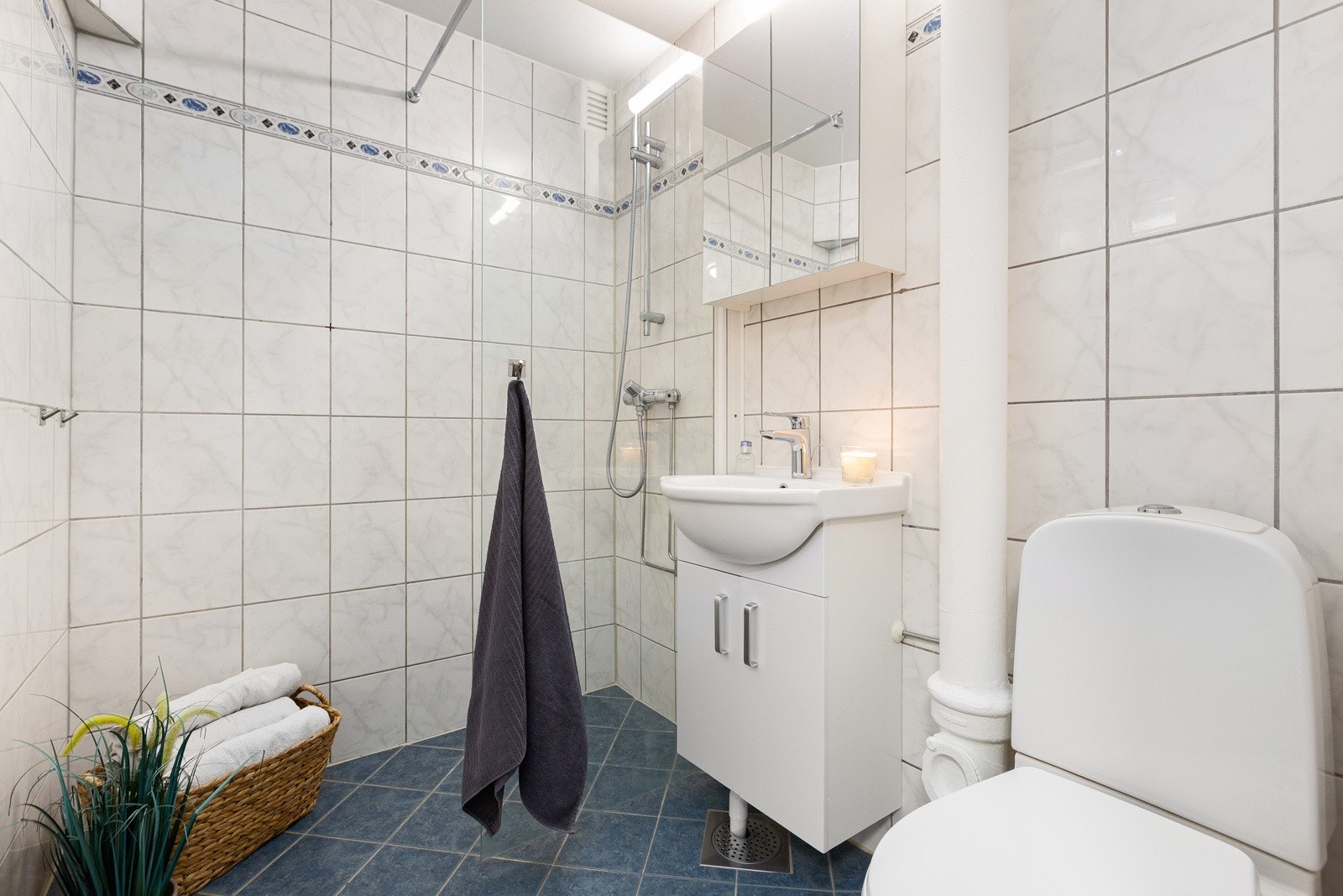 Badet har fliser på gulv og vegger. Her er det dusjsone, servant og wc. Galleribilde