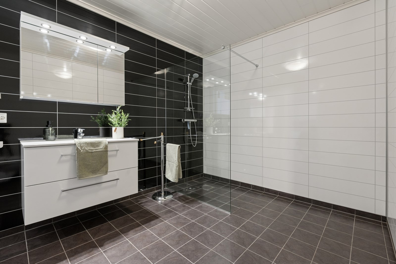 Rommet er innredet med et vegghengt toalett, baderomsmøbel med vask, speilskap, høyskap og en dusjvegg i glass. Galleribilde