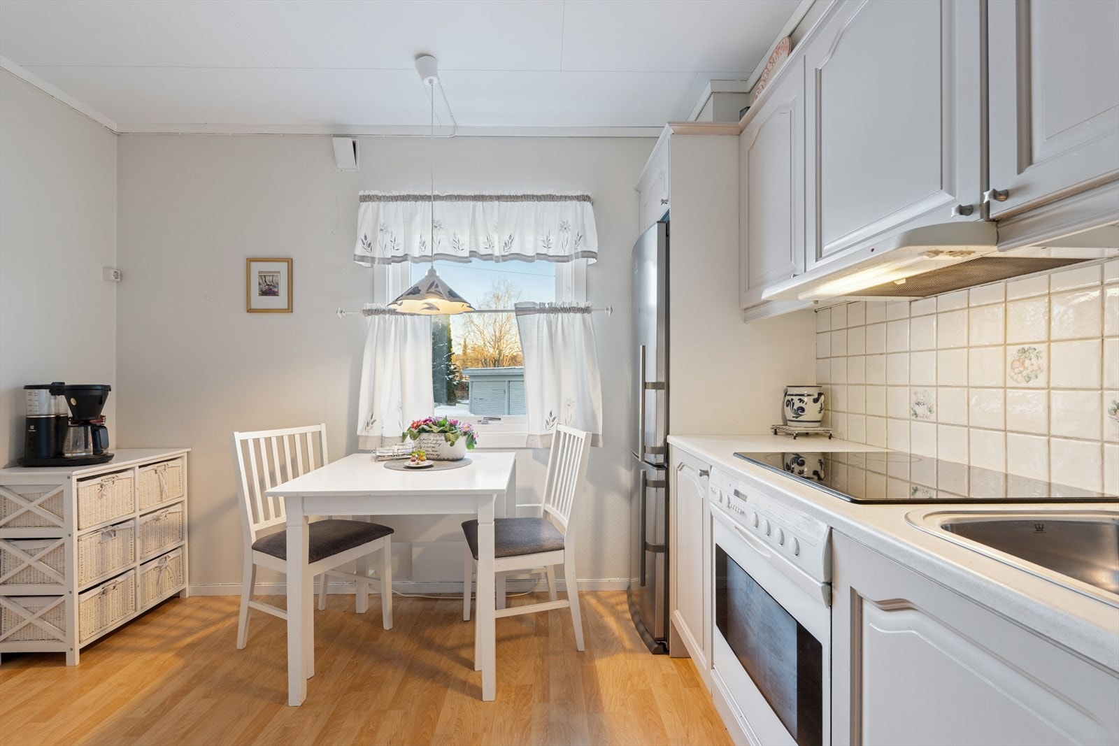 Over oppvaskbenken er det fliser som gir god beskyttelse mot vannsprut, og over koketoppen finner du en kjøkkenventilator med avtrekk ut Galleribilde