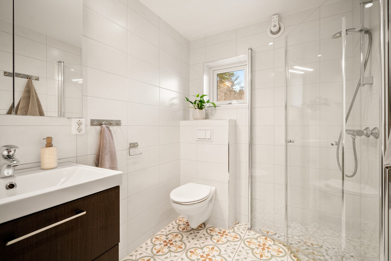 Lyst og pent bad, med vegghengt toalett, dusjhjørnet og servant med innredning. Galleribilde