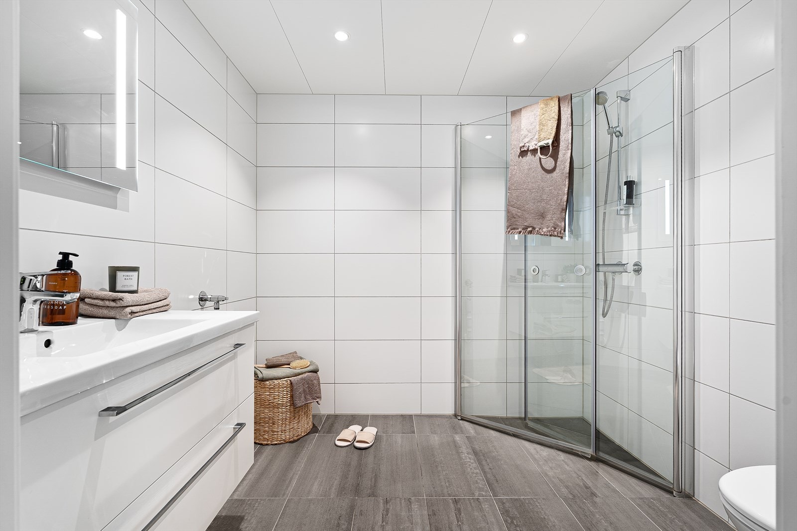 Flislagt baderom utstyrt med varme i gulv, innfellbare dusjvegger, opplegg for vaskemaskin, toalett, servant med oppbevaring og speil. Galleribilde