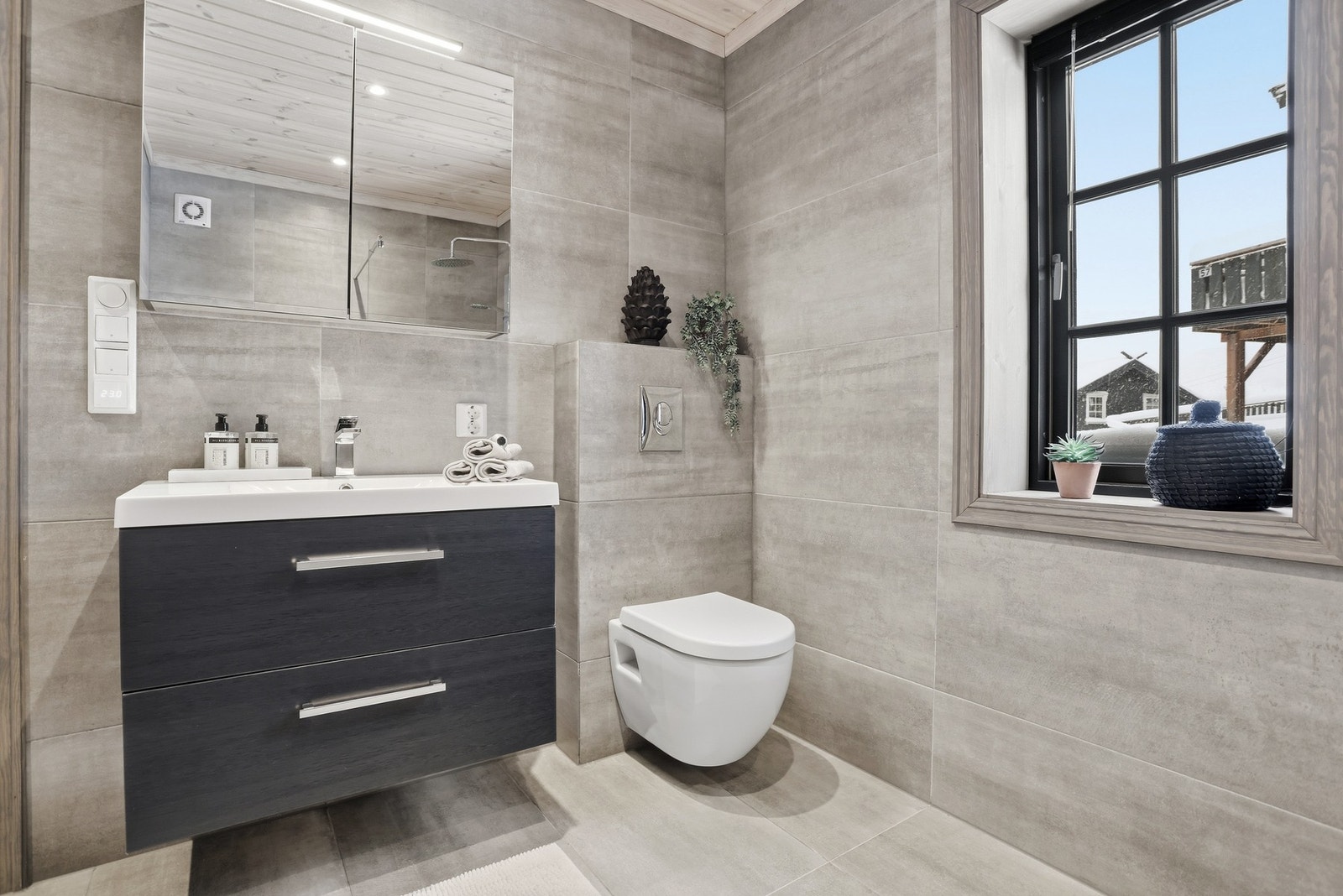 Baderom i hovedetasjen - badet inneholder vegghengt toalett, innredning med servant og speilskap, dusj med glassdører og waterfall armatur, og tilgang til badstue Galleribilde