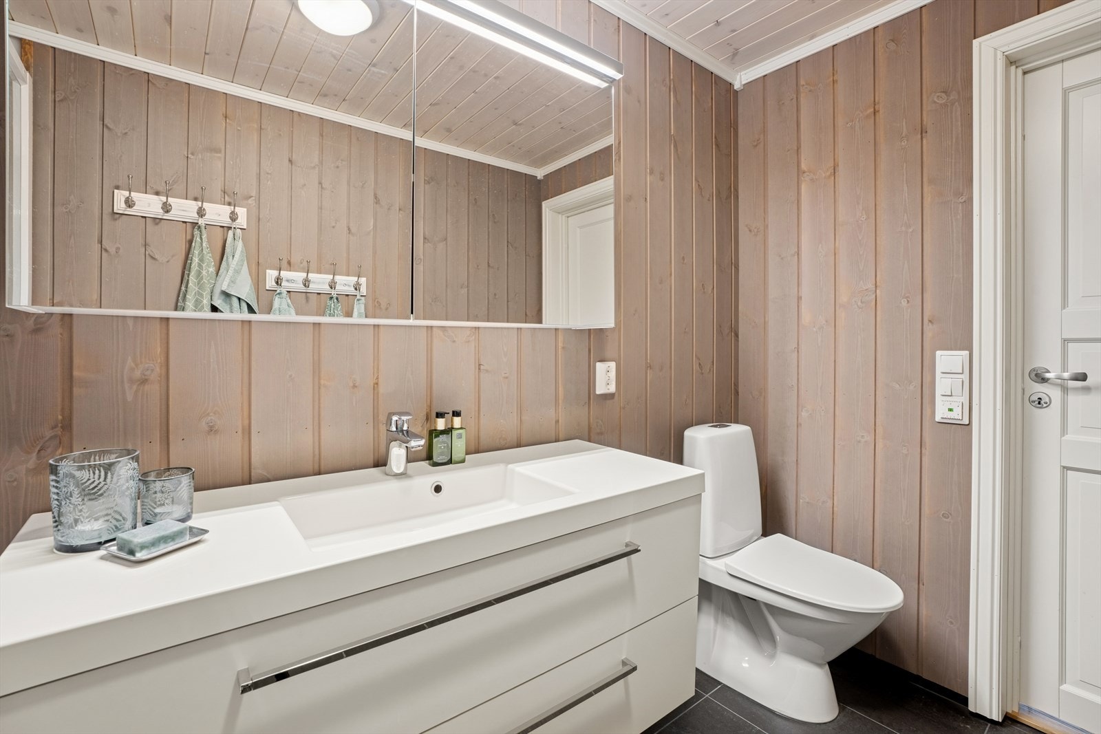 Badet er innredet med gulvstående toalett, dusjkabinett og servantinnredning, samt speilskap med integrert belysning. Det er opplegg for vaskemaskin. Galleribilde