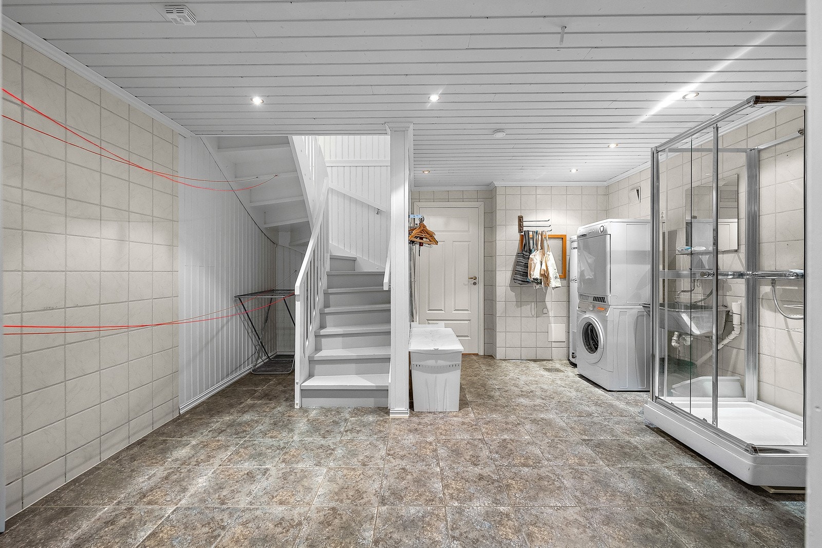 Fra hallen i 1. etasje er det trapp ned til bad/vaskerom i kjelleren. Rommet er romslig og praktisk, med god plass til både oppbevaring og tørking av klesvask. Galleribilde