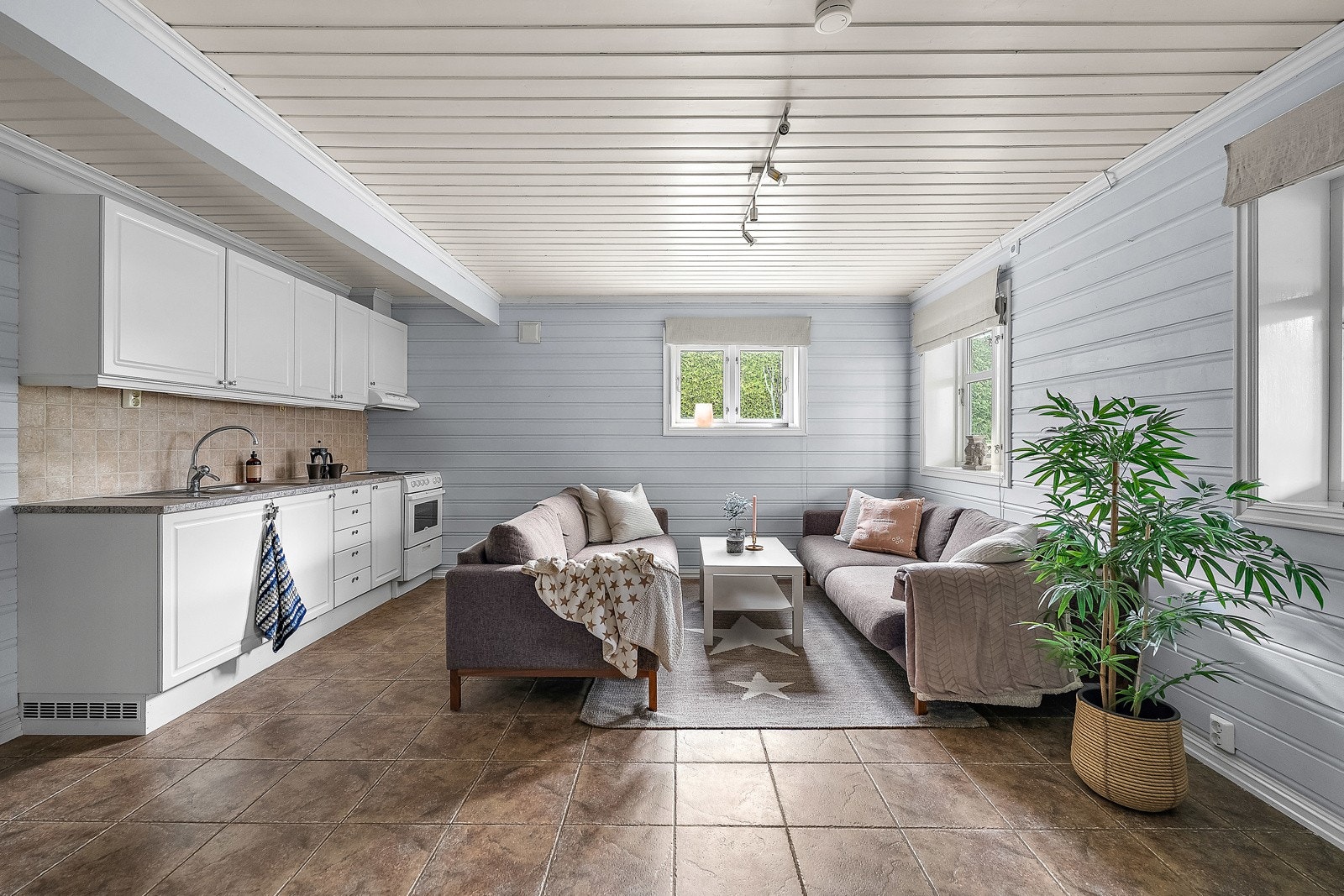 Kjellerstue med kjøkkeninnredning med fabrikkmalte fronter, laminat benkeplate, oppvaskkum, ventilator, fliser over benk og belysning under overskap. Galleribilde