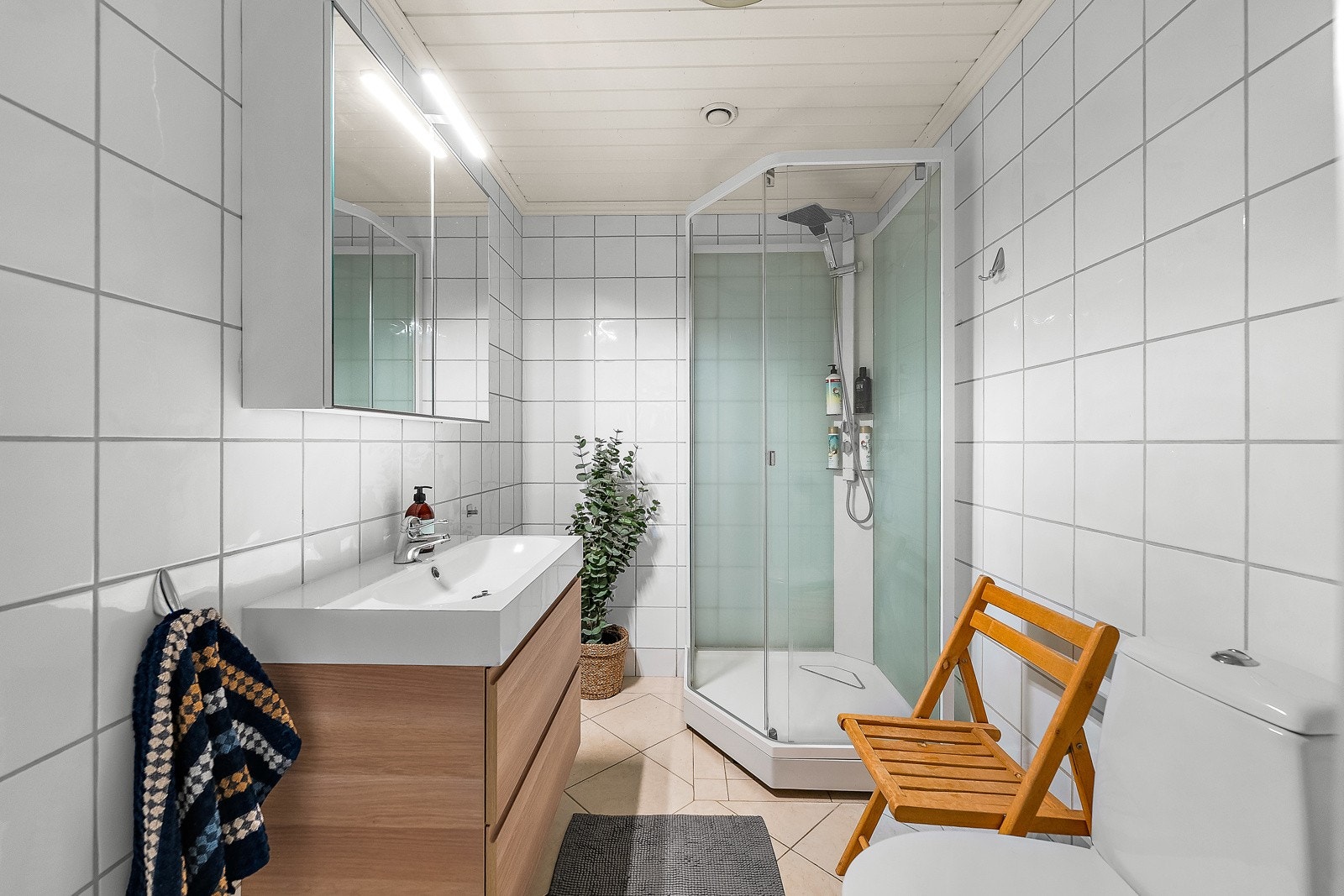 Kombinert bad/vaskerom i utleiedelen med fliser på gulv og vegger, opplegg for vaskemaskin, toalett, dusjkabinett i herdet glass, speilskap med belysning og baderomsinnredning med finerte fronter og heldekkende servant. Galleribilde