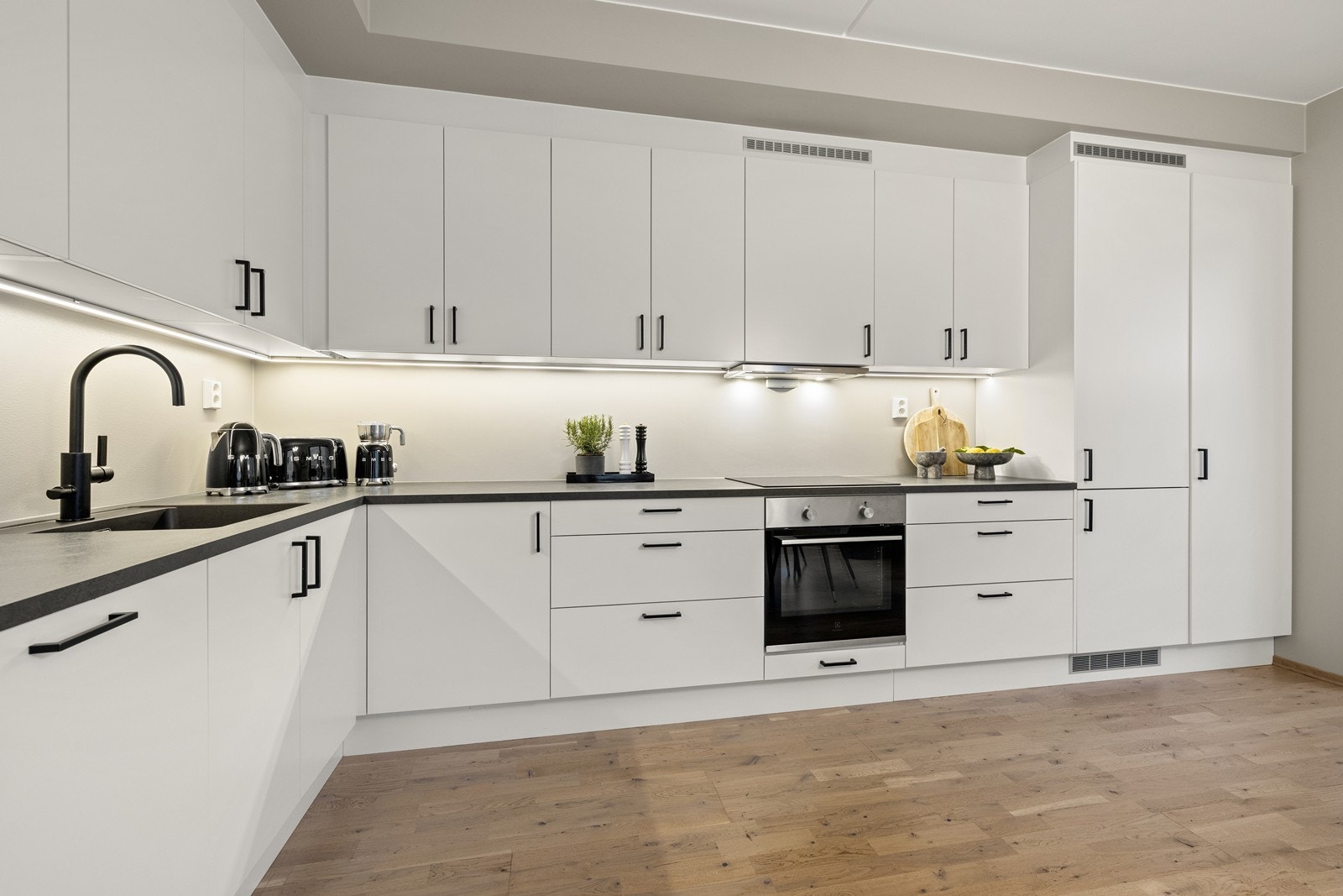 Kjøkkeninnredning med slette fronter, mørk benkeplate og integrerte hvitevarer. Galleribilde