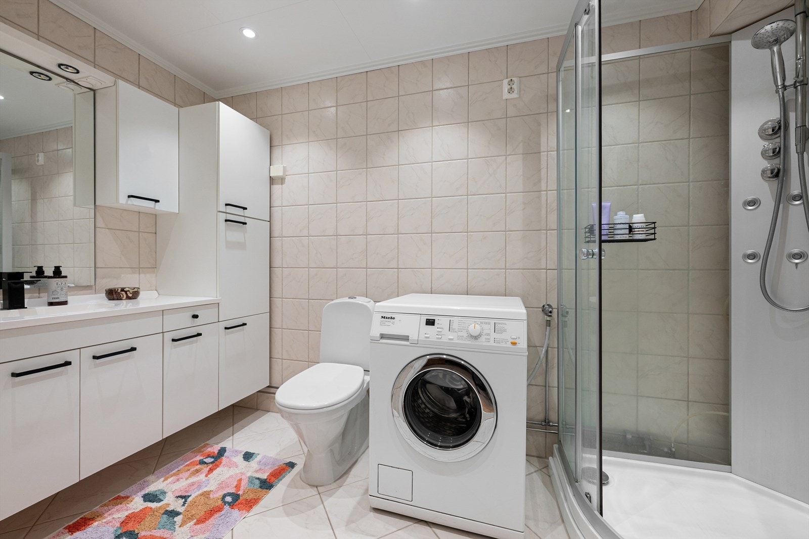 Badet er utstyrt med toalett, dusj og opplegg for vaskemaskin og tørketrommel samt servantinnredning med over- og underskap. Galleribilde