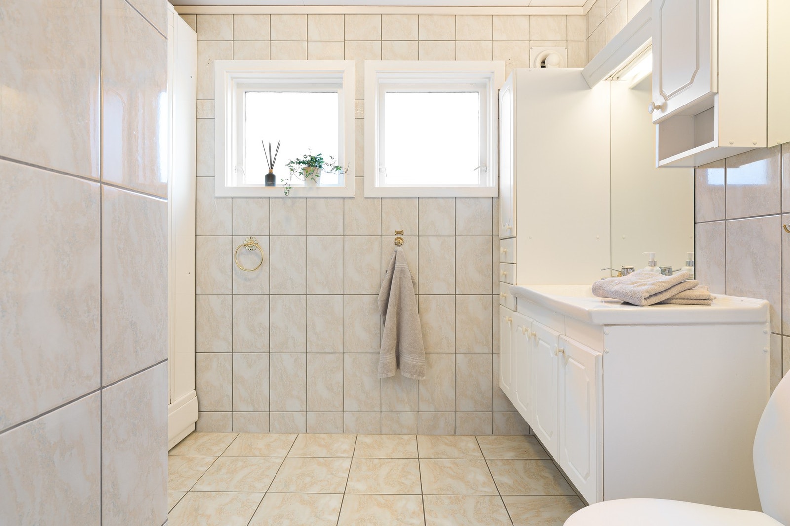 Badet har lyse fliser på både gulv og vegger. Rommet er innredet med servantskap, høyskap og speil. Galleribilde