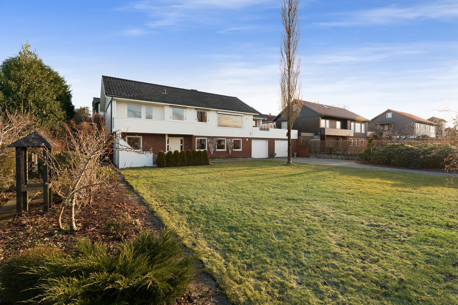 Den er beplantet med prydbusker, blomsterbed og plenareal Galleribilde