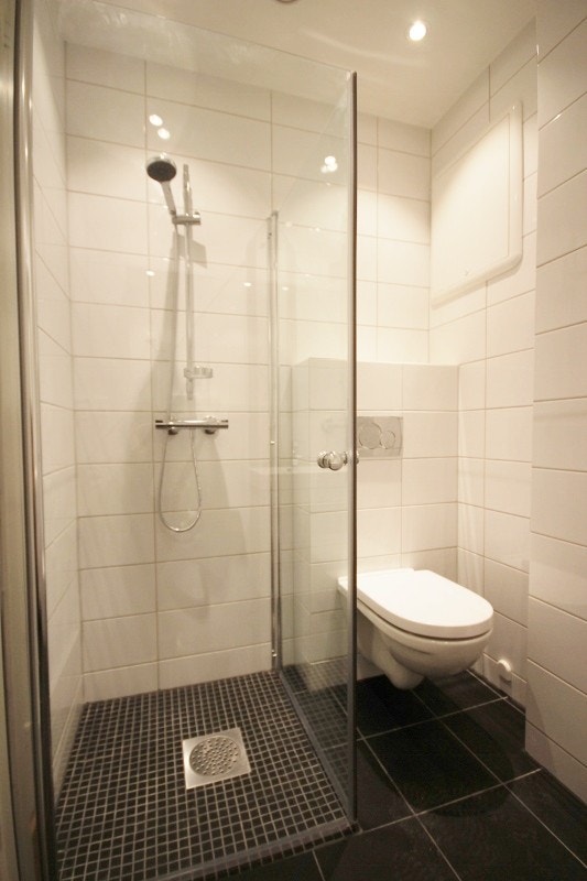Flislagt bad med vegghengt toalett, dusjhjørne med glassdører og servant med underskap. Galleribilde