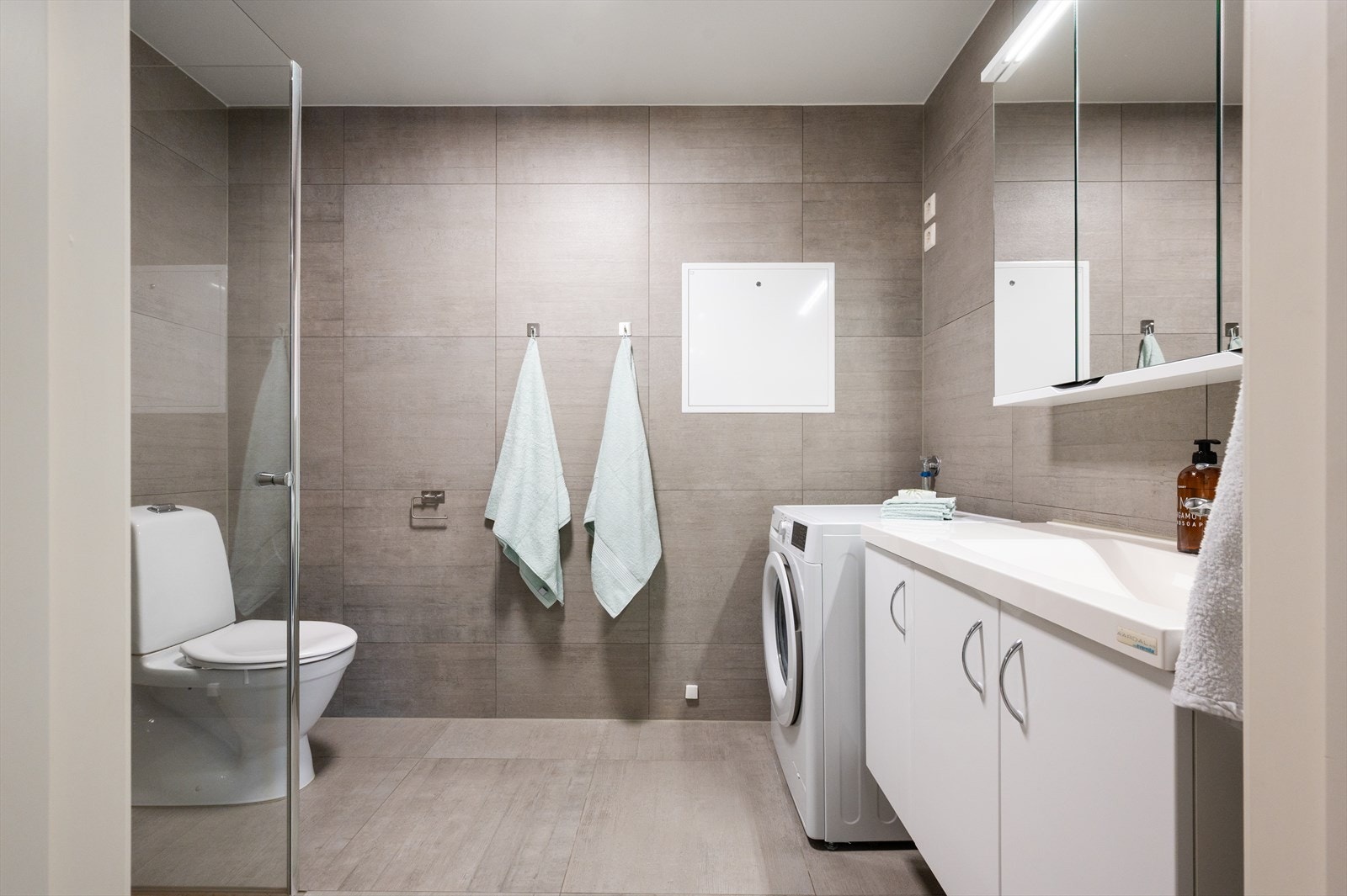 Pent flislagt bad fra byggeår 2017. Baderomsinnredning bestående av benkeskap med slette fronter og speilskap over servant med belysning. Galleribilde