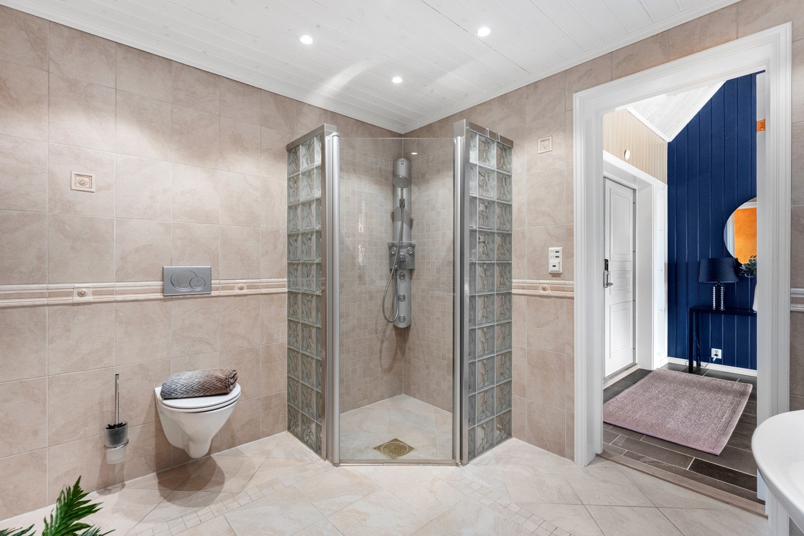 Rommet er innredet med vegghengt toalett, dusjhjørne med glassbyggerstein og servant med underskap og speil Galleribilde