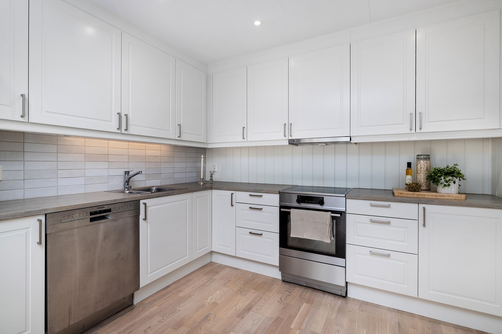 Hvit kjøkkeninnredning med profilerte fronter. Benkeplen er av laminat. Vegg over kjøkkenbenk er flissatt. Spotter i taket. Galleribilde