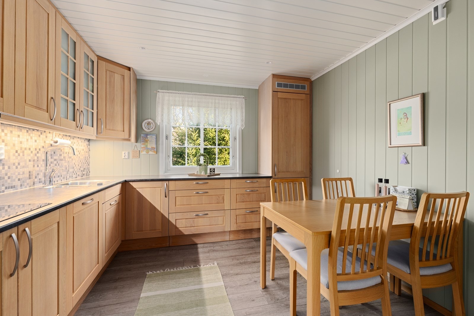 Her er det fliser mellom benkeplate og overskap på én vegg, perfekt for å beskytte veggen mot vann og matsprut. Kjøkkenet er utstyrt med komfyrvakt og automatisk vannstoppesystem. Ventilator med avtrekk ut. Galleribilde