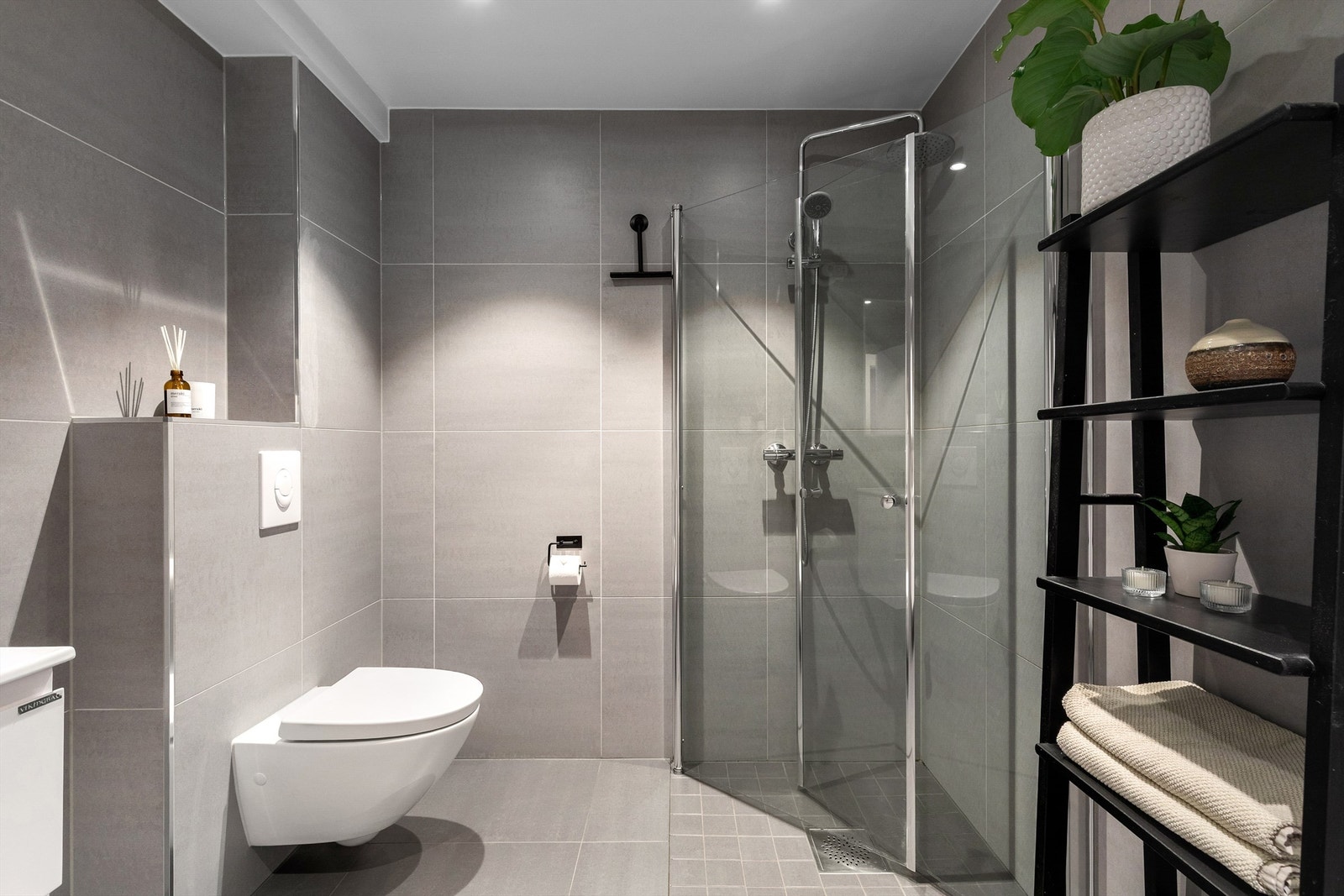 Dusjhjørnet har plassbesparende svingbare dører i glass og armatur med regnfallsdusj og håndholdt dusj Galleribilde