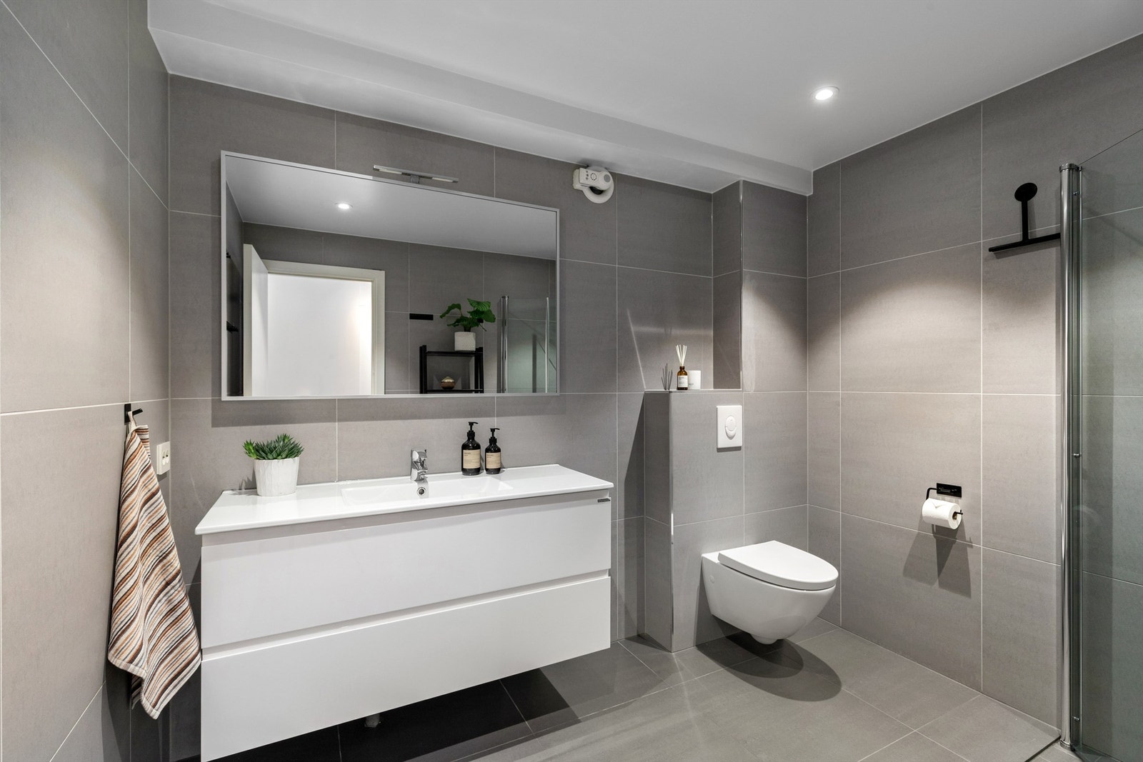 Romslig flislagt bad med gulvvarme. Badet er holdt i moderne farger, med store fliser på vegg og gulv Galleribilde