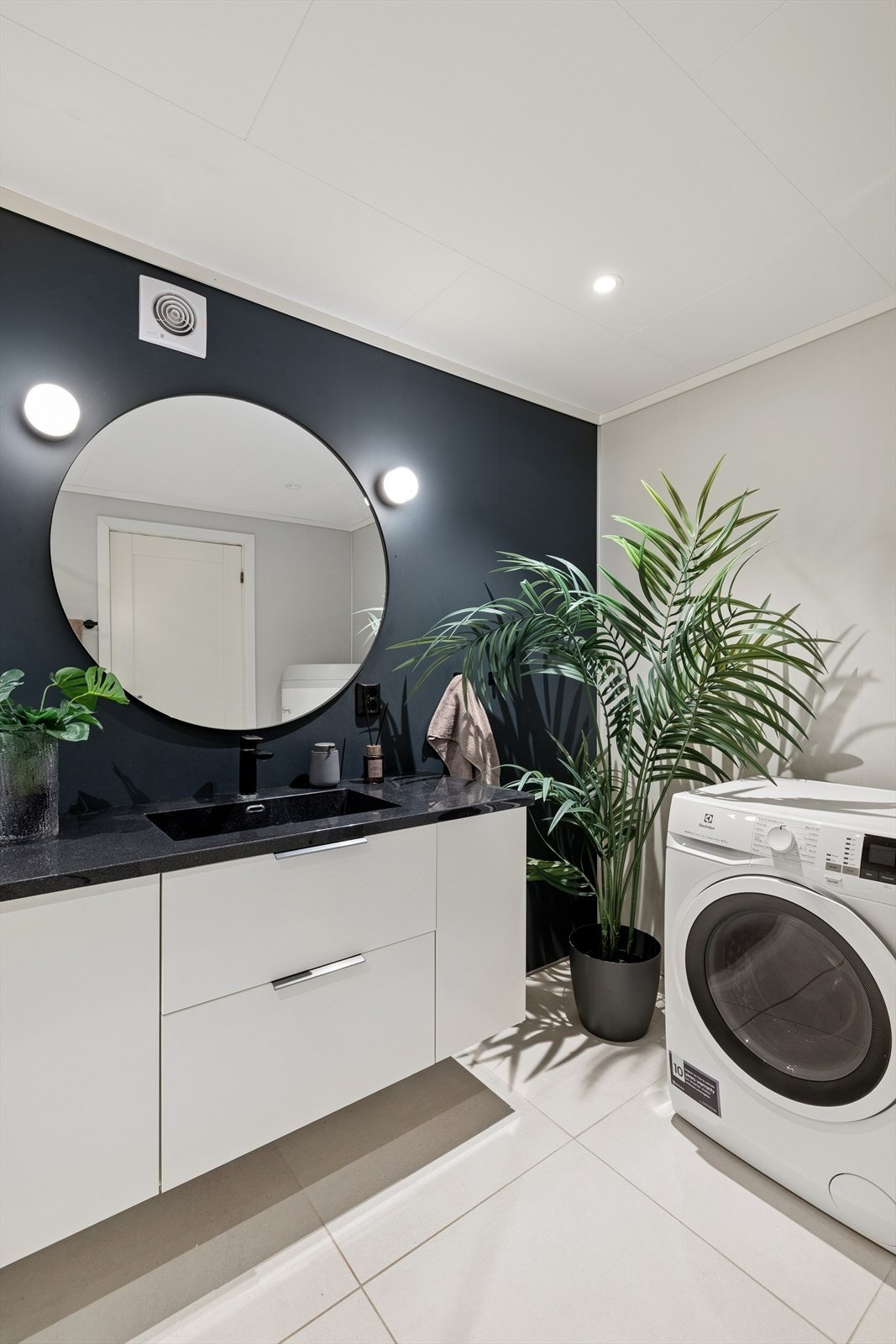 Badet er innredet med en servant med tilhørende underskap, speil med belysning, vegghengt toalett, dusjnisje og opplegg for vaskemaskin. Ventilasjonen med mekanisk avtrekk og tilluft via dør. Galleribilde