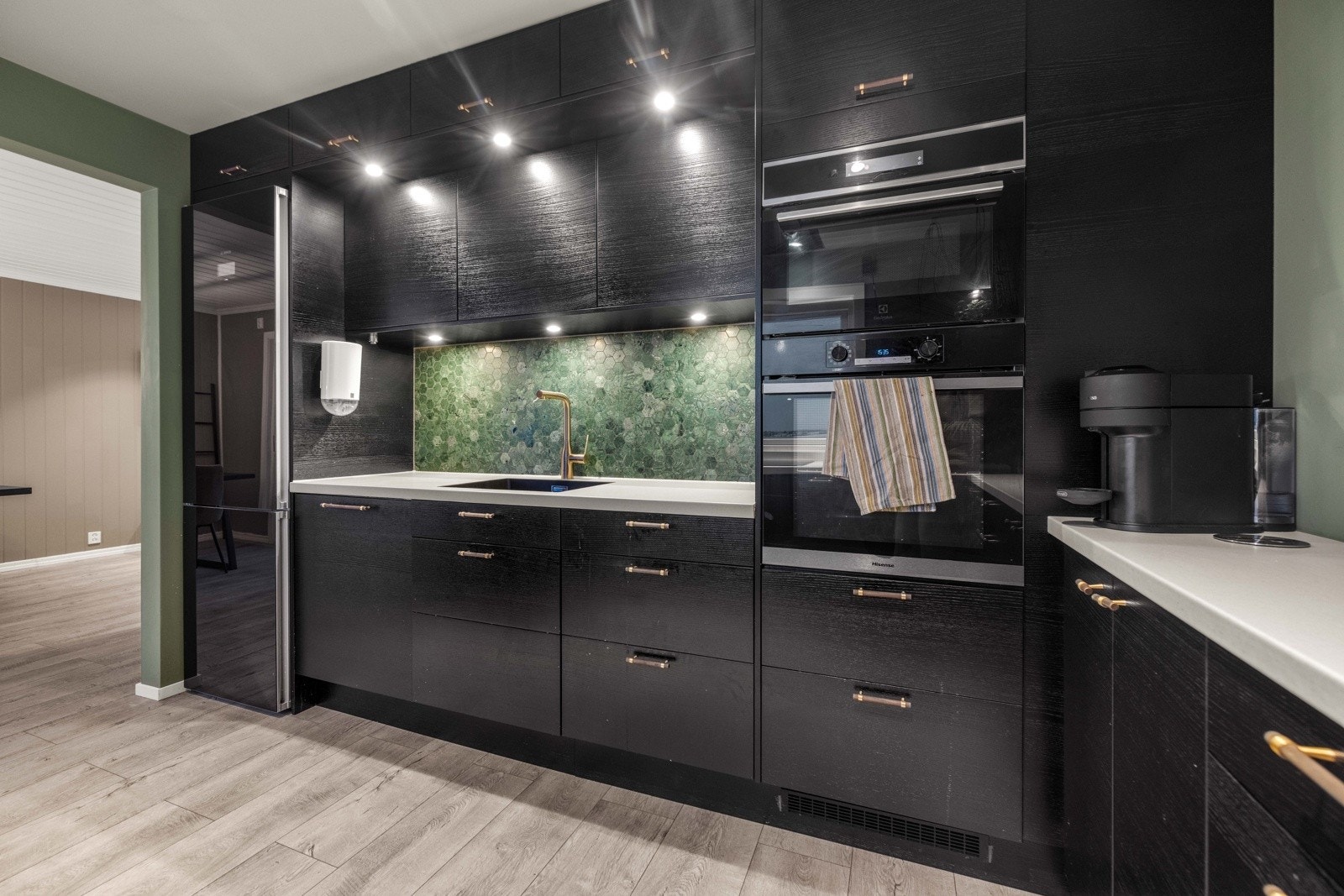 Moderne innredning med sorte fronter med trestruktur og laminert benkeplate med nedfelt oppvaskkum. Galleribilde