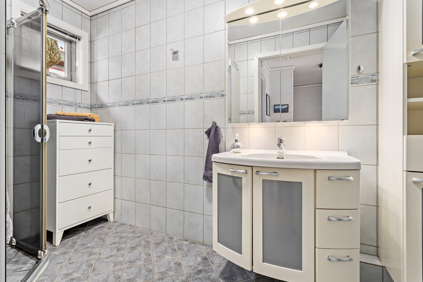 Innreiing består av baderomsmøbel med heildekkande servant, vegghengt toalett og dusjhjørne med skyvedører. Galleribilde