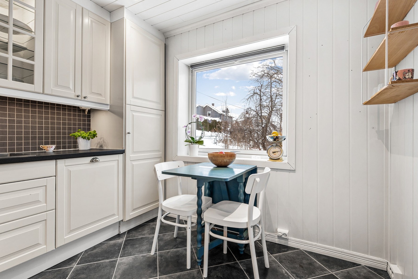 Det er fliser på vegg mellom benk og overskap, samt montert ventilator med avtrekk over platetopp Galleribilde