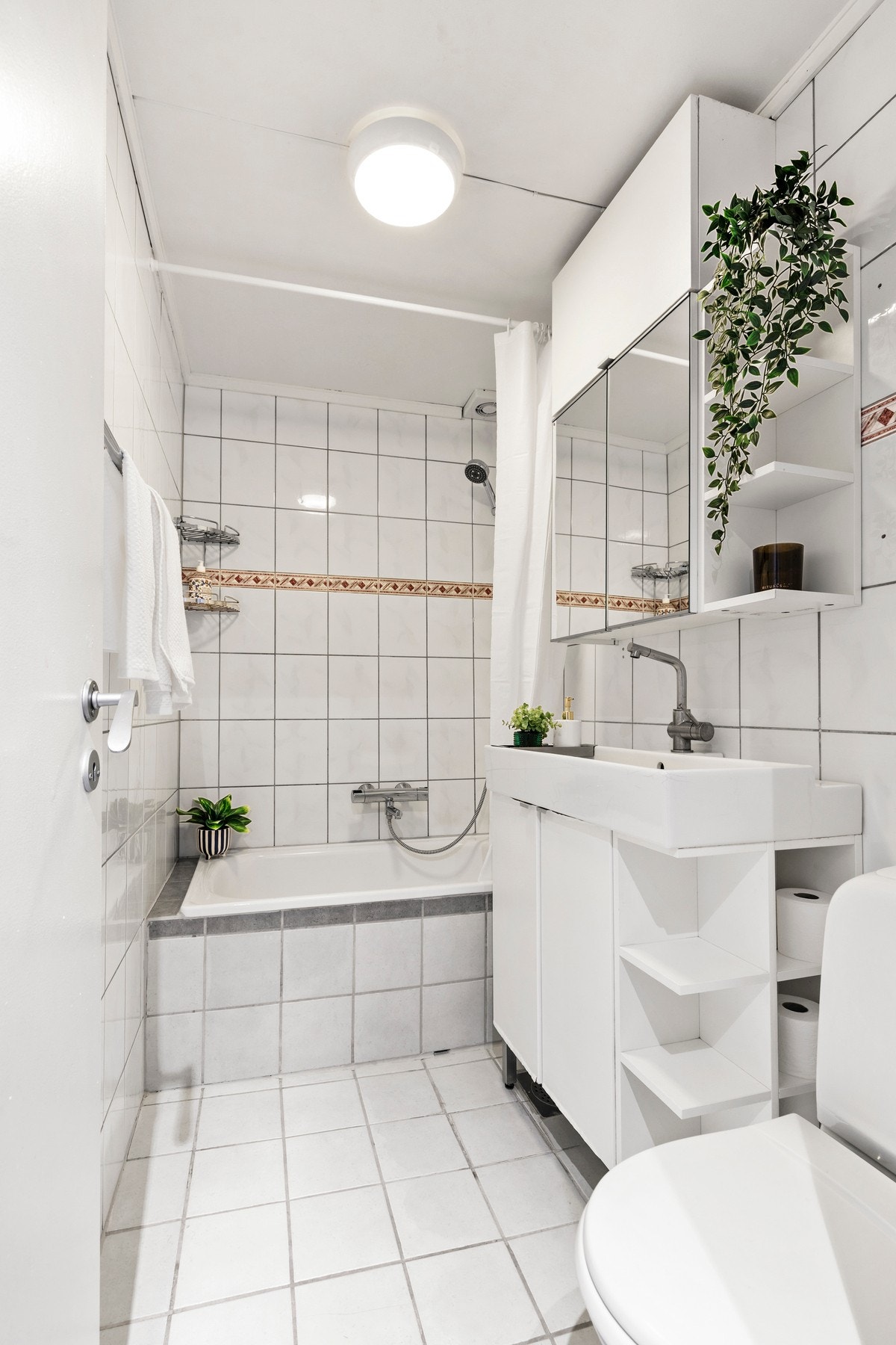 Rommet er utstyrt med gulvstående toalett, servantskap med heldekkende servant og ett-greps blandebatteri, speilskap og innebygget badekar Galleribilde