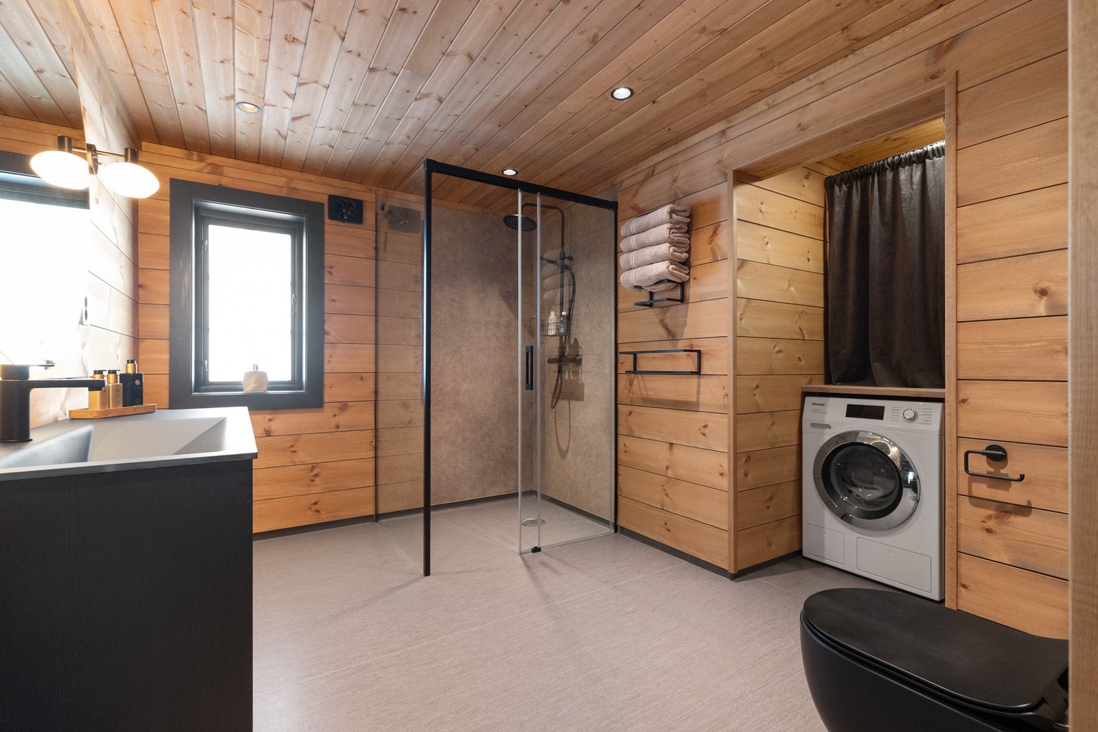 Bad har montert servant, vegghengt klosett, opplegg til vaskemaskin og utslagsvask med kran av stål Galleribilde