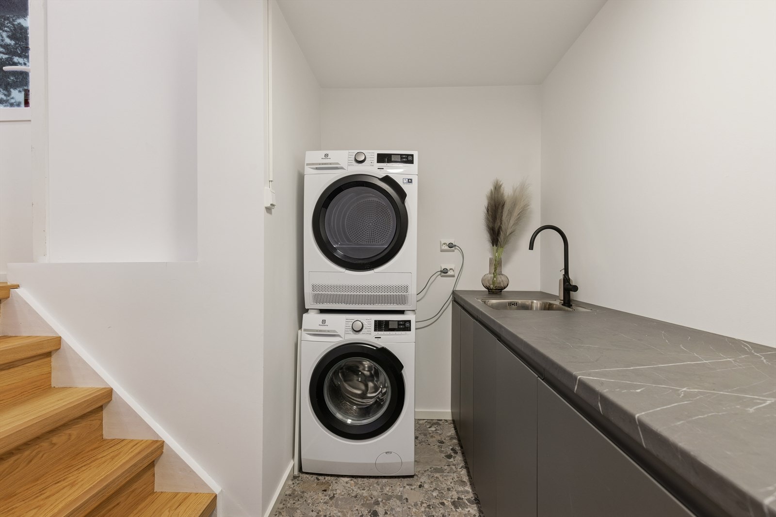 Praktisk vaskerom med opplegg for vaskemaskin og god plass til tørketrommel. Rommet er utstyrt med benkeinnredning med vaskekum og kjøkkenkran, som gir gode arbeidsforhold. Galleribilde