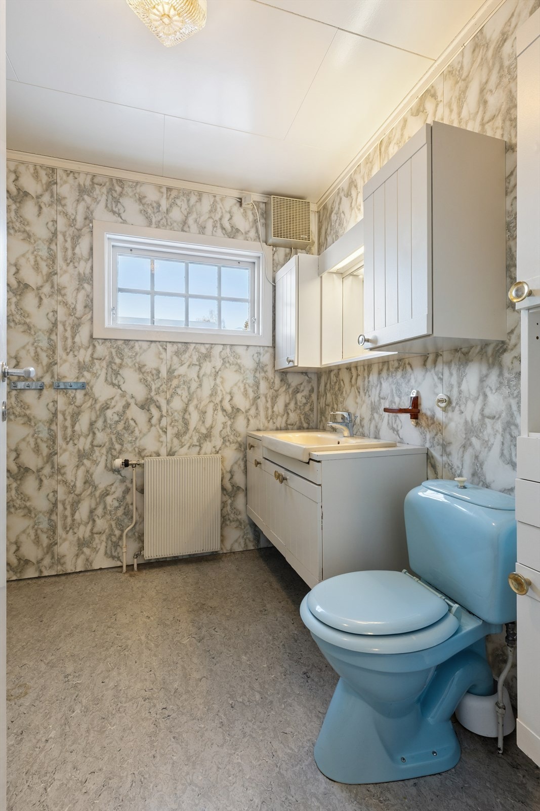 Baderommet har vinylbelegg på gulvet og tapetserte vegger, med radiator for oppvarming, fra byggeår. Galleribilde