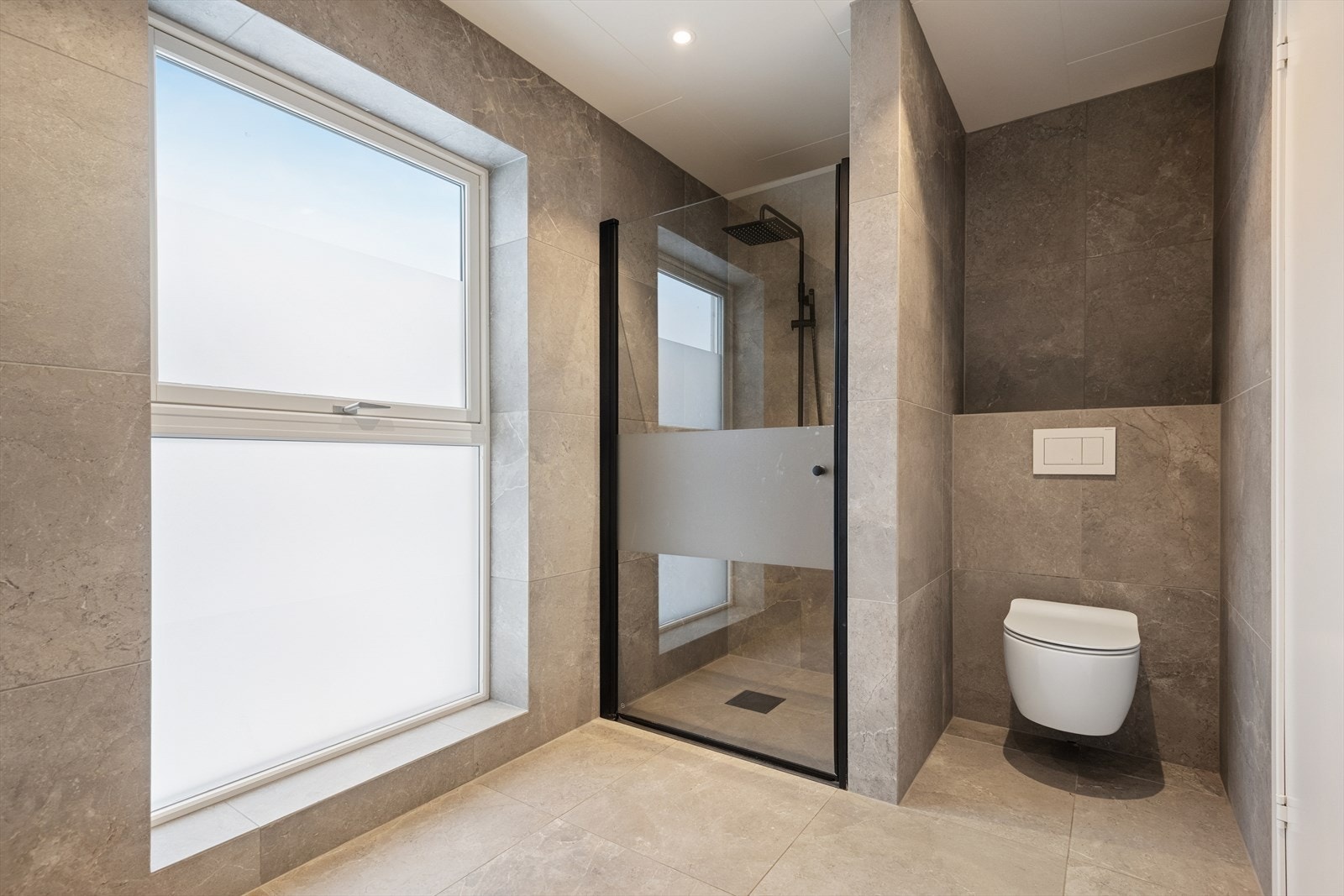 Badet er innredet med en baderomsinnredning med nedfelt servant, veggmontert toalett og et dusjhjørne med glassvegg. Galleribilde