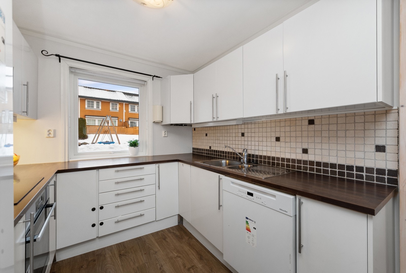 Hvit glatt kjøkkeninnredning med laminat benkeplate. Fliser mellom benk over overskap. Galleribilde