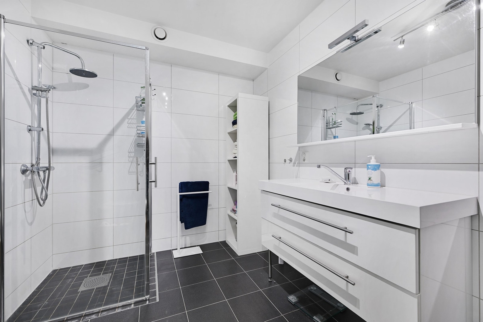 Delikat, flislagt baderom med vegghengt toalett, servant i stilren baderomsinnredning og dusj. Galleribilde