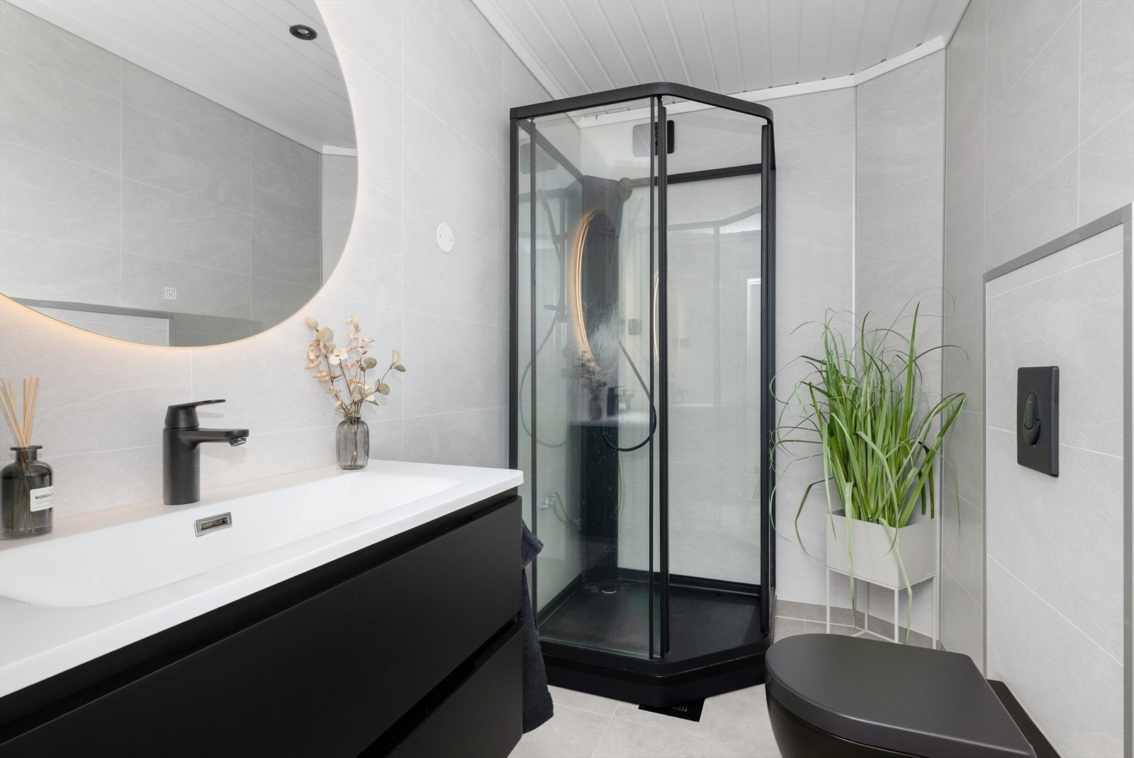 Badet er innredet med vegghengt toalett, dusjkabinett og servantinnredning med skuffer og speil. Galleribilde