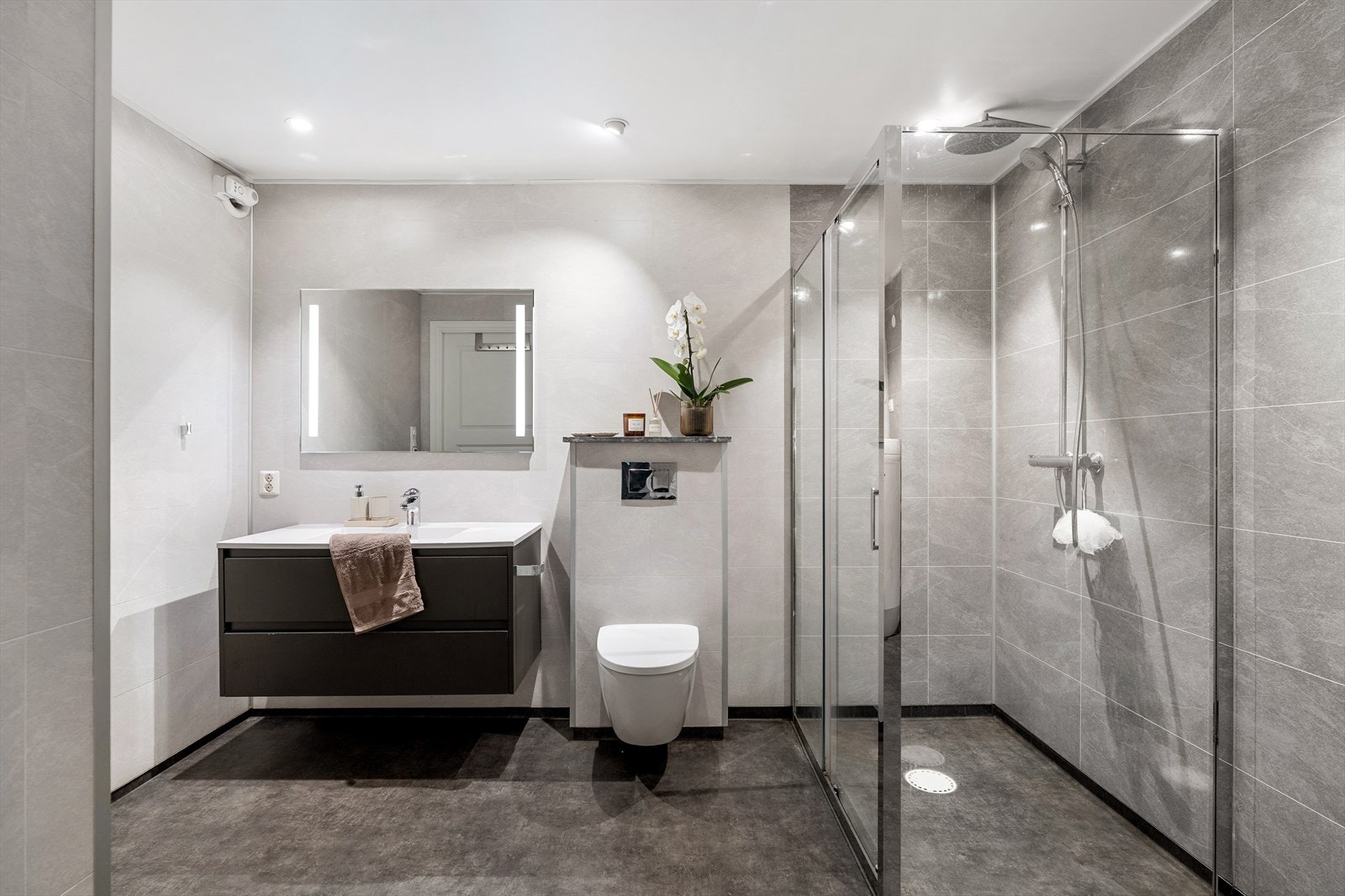 Pent baderom innredet med nedfelt servant, vegghengt toalett og romslig dusjnisje. Galleribilde