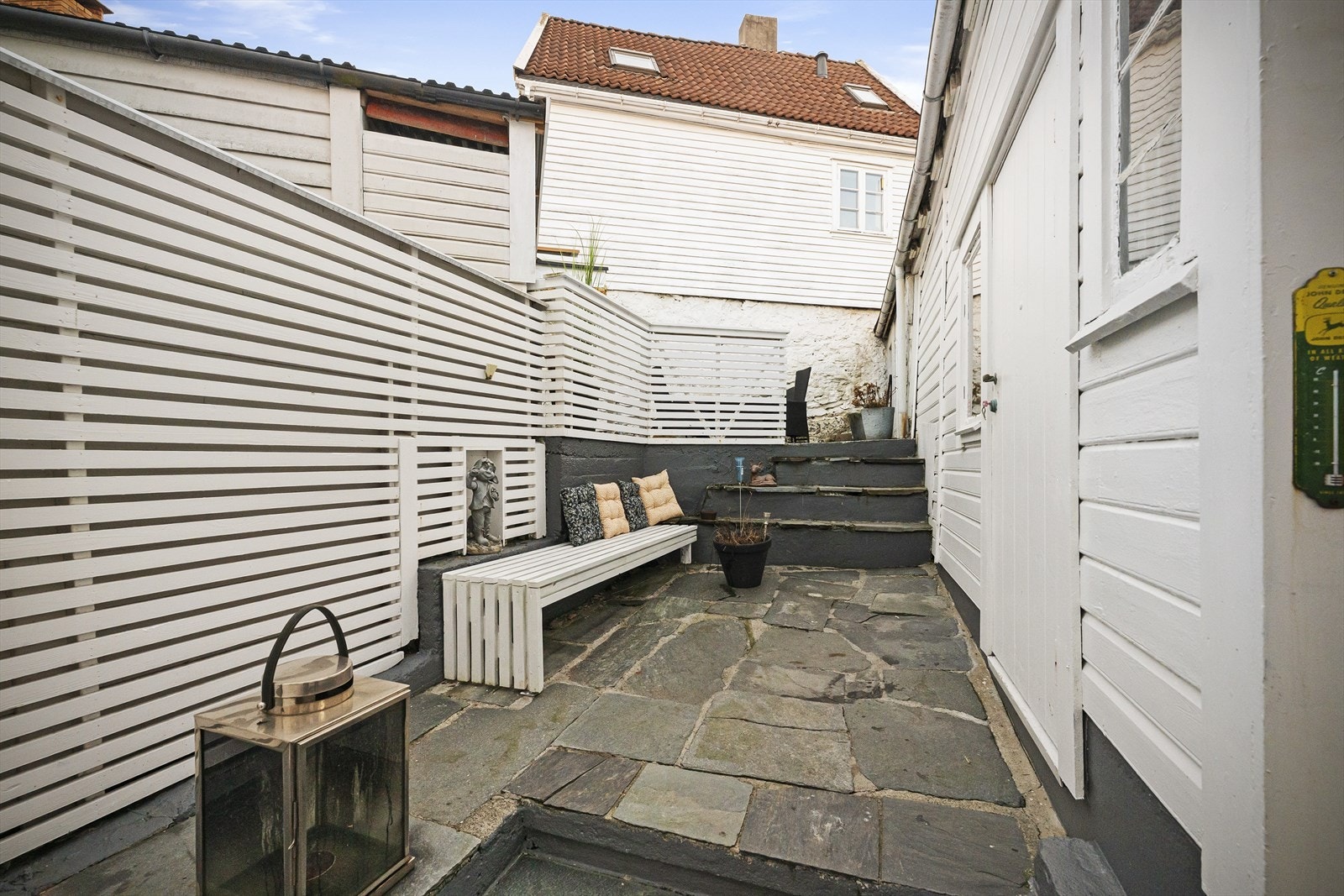 Sjarmerende og privat uteplass med steinheller og hvite detaljer. Perfekt for avslapning og sosiale sammenkomster i rolige omgivelser. Galleribilde