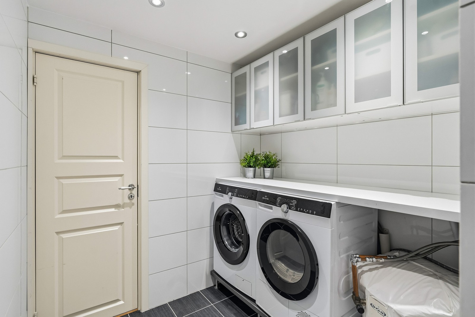 Meget praktisk vaskesone med opplegg og plass for vaskemaskin og tørketrommel - Videre utstyrt med praktisk arbeidsbenk og vegghengte skap Galleribilde