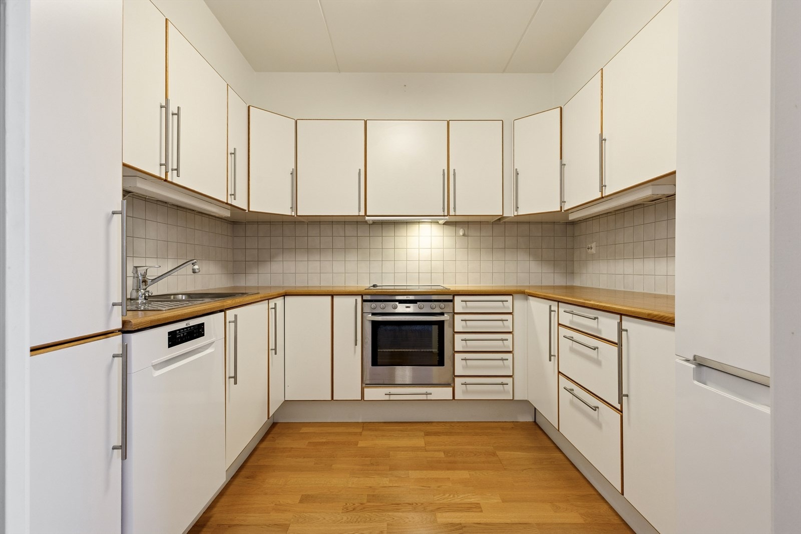 Kjøkkenet er stilrent innredet med hvite, slette fronter og trefarget benkeplate i laminat. Et godt utnyttet kjøkken hvor man har godt med skap- og skuffeplass, samt gode arbeidsflater på benk. Galleribilde