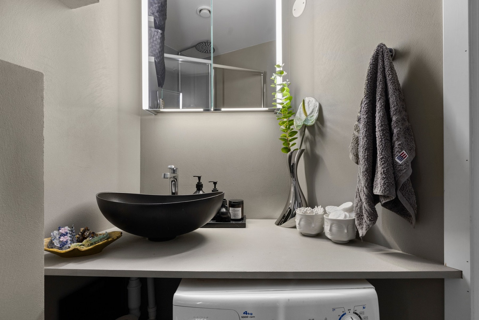 Benkeplate med microsement og utenpåliggende vask med ett-greps armatur i krom.
Veggmontert speilskap med integrert belysning. Galleribilde