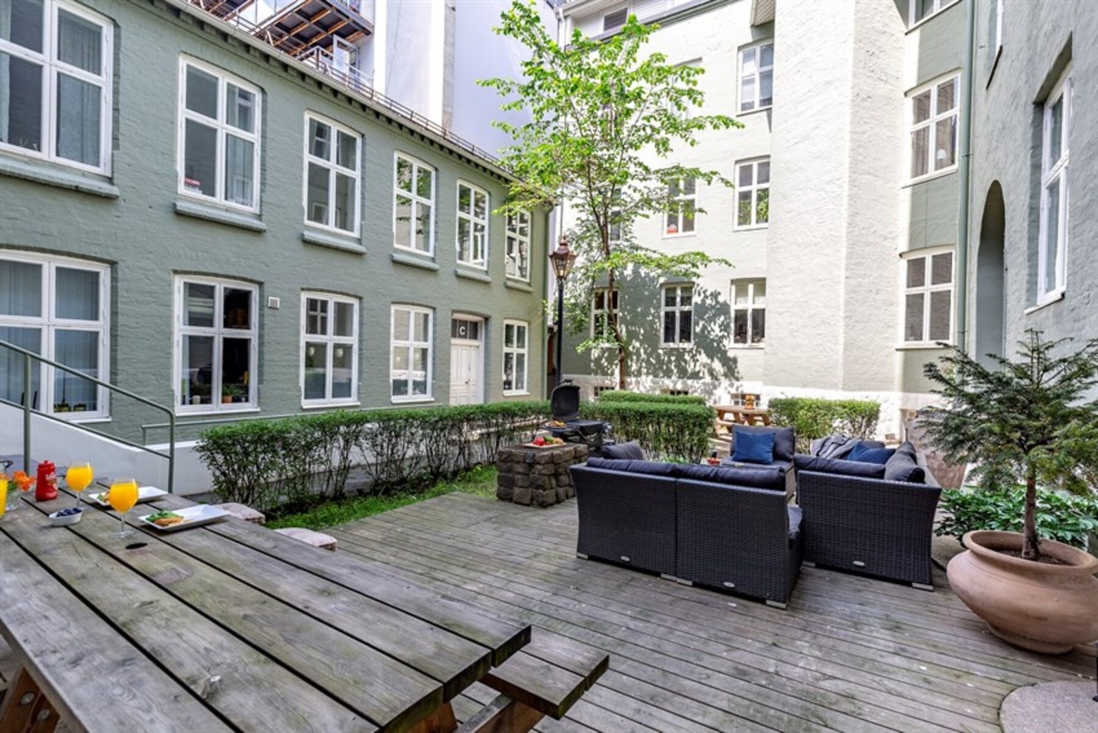 Pent opparbeidet bakgård sommertid med terrasseplatting, grillplass og sittegrupper samt noe beplantninger Galleribilde