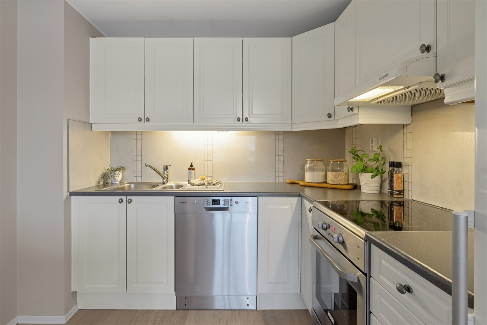 Over benkeflaten i laminat er det lagt fliser på vegg, og kjøkkenet er utstyrt med nedfelt kum i rustfritt stål. Her finner du frittstående hvitevarer som komfyr med platetopp, kjøle-/fryseskap og oppvaskmaskin. Galleribilde