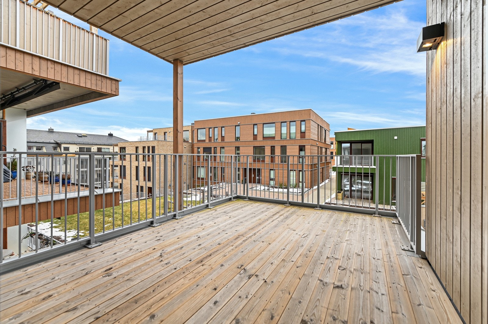 Den romslige balkongen med tredekke og metallrekkverk gir utsikt over nærområdet. Et perfekt sted for morgenkaffe eller ettermiddagshygge. Galleribilde