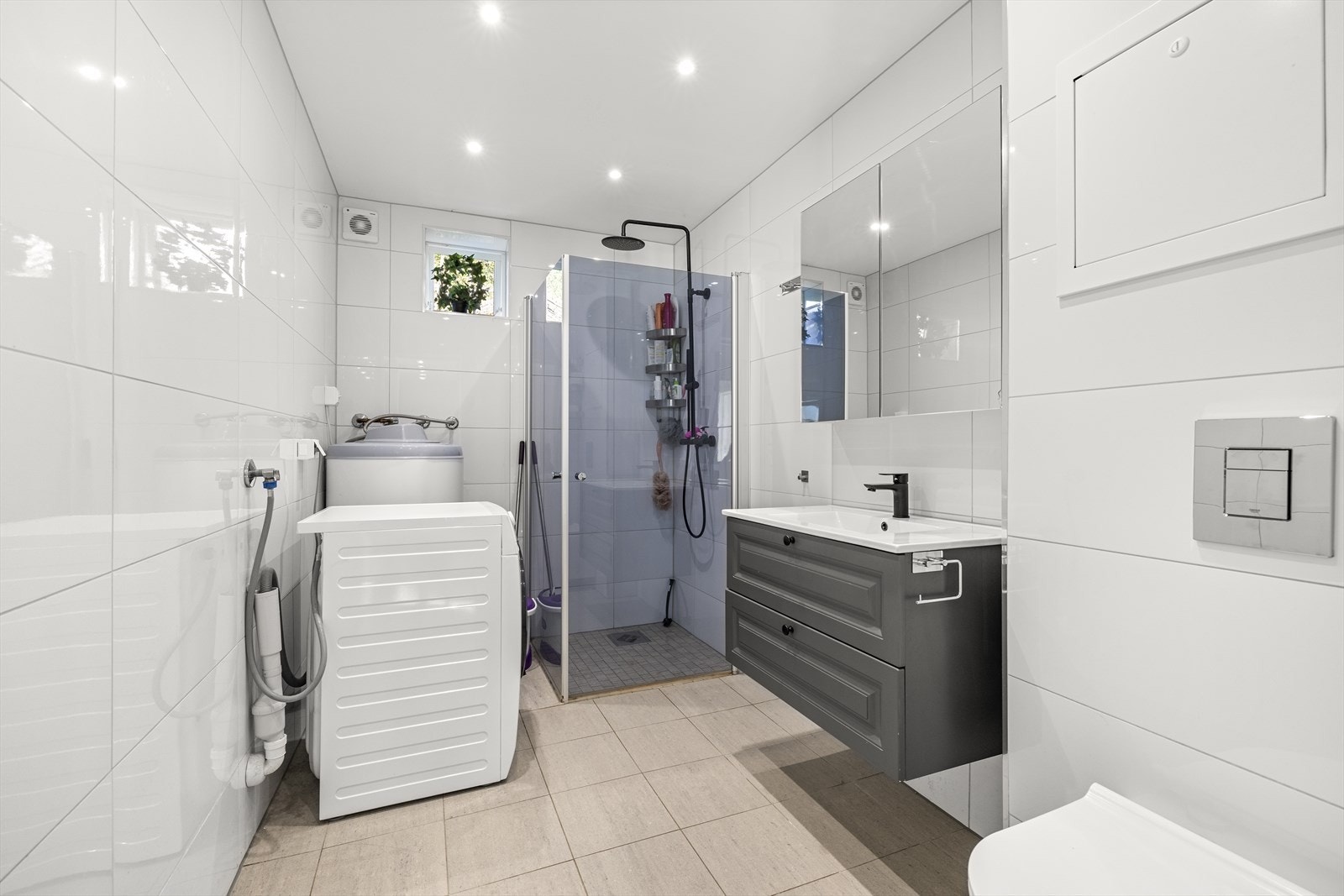 Lyst og flislagt baderom som ble renovert i 2022. Badet er innredet med vegghengt toalett, servant med underskuffer, speilskap, dusjhjørne med regnfallsdusj og innfellbare glassdører, og opplegg for vaskemaskin. Galleribilde