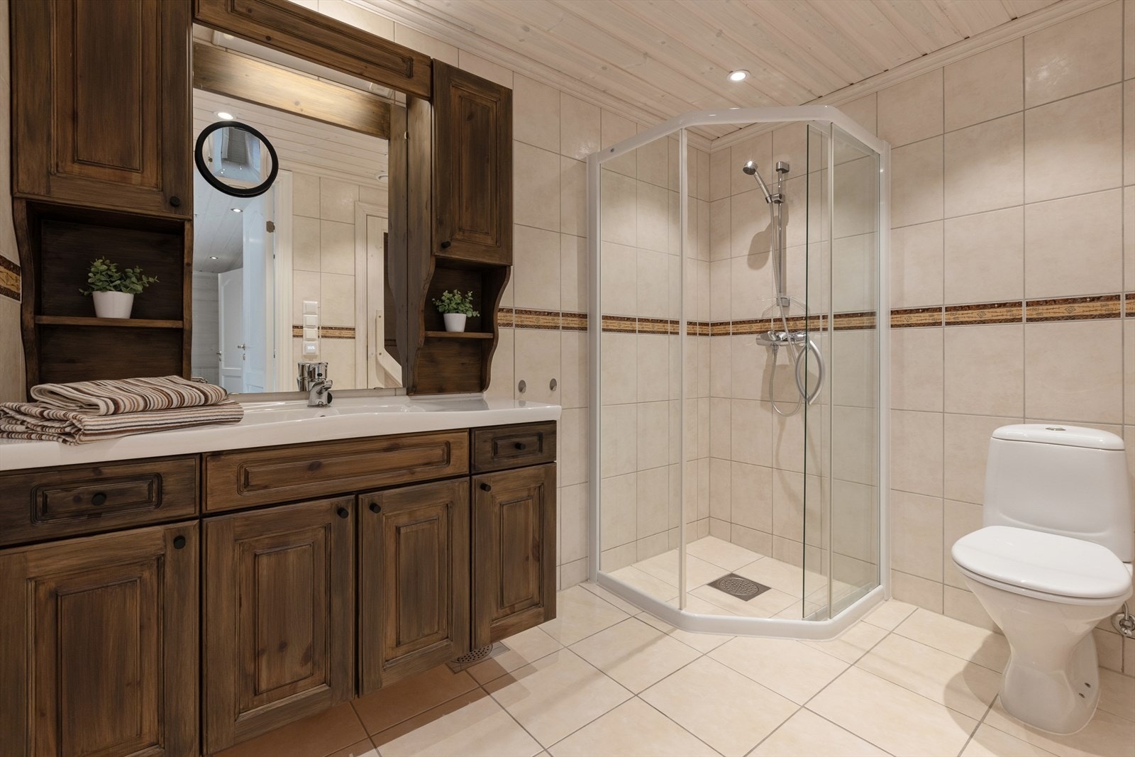 Baderommet i underetasjen er innredet med lyse fliser på gulv og vegger. Også her har man varmekabler i gulvet. Badet er ellers utstyrt med dusjhjørne, toalett og baderomsinnredning med nedfelt servant. Galleribilde