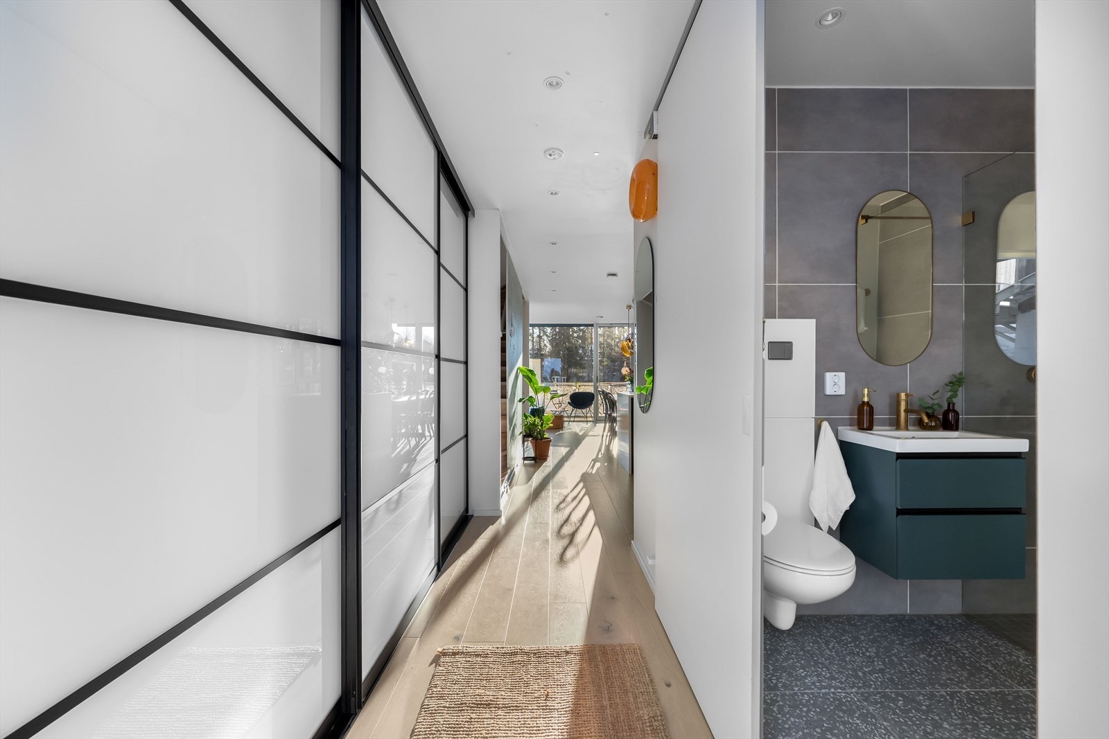 Innenfor døren møtes du av en romslig og lys gang med god plass til både sko og yttertøy i en lekker skyvedørsgarderobe med glatte fronter og sorte detaljer Galleribilde