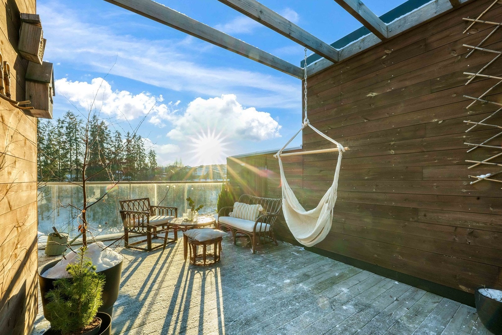 Takterrasse med terrassebord, glassrekkverk og levegg med liggende kledning, samt stemningsfull pergola Galleribilde